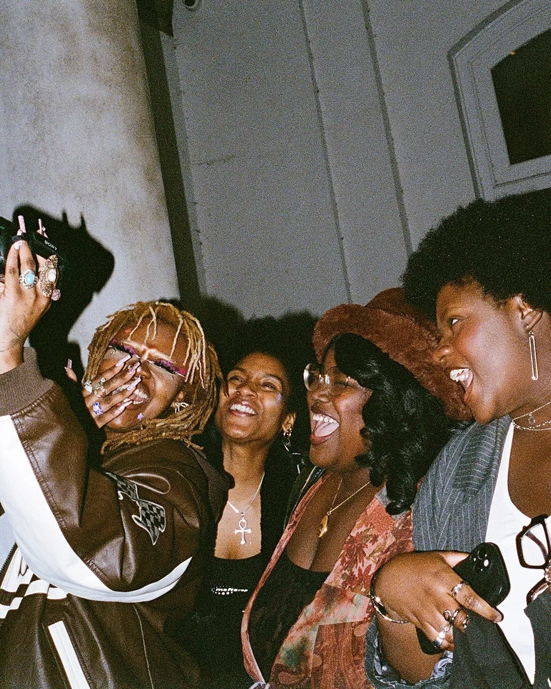Group of five women smiling, laughing, and taking a selfie together at a party or gathering.