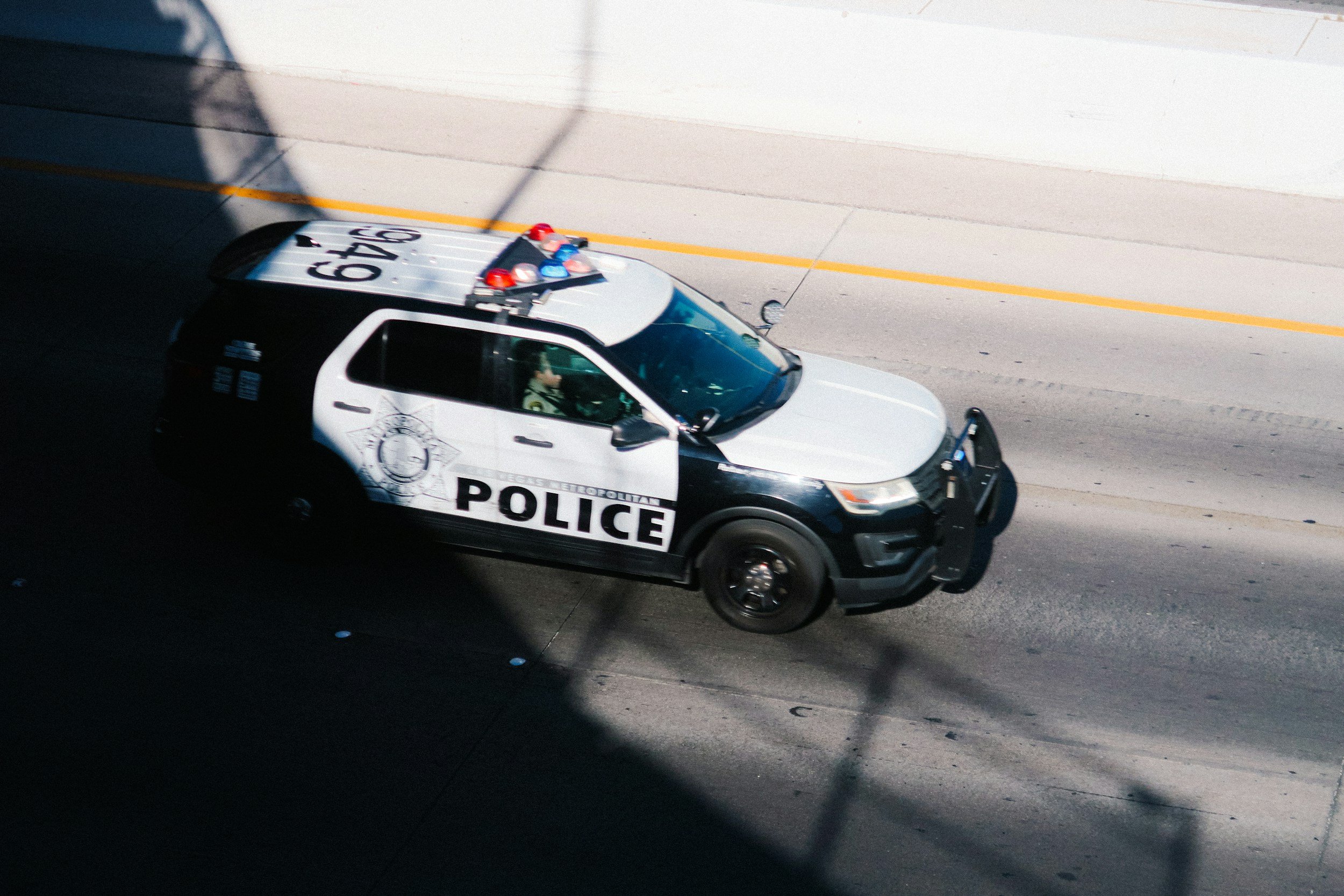 A Las Vegas Metropolitan Police car driving on a highway, partially in shadow, with a white and black color scheme and police markings.