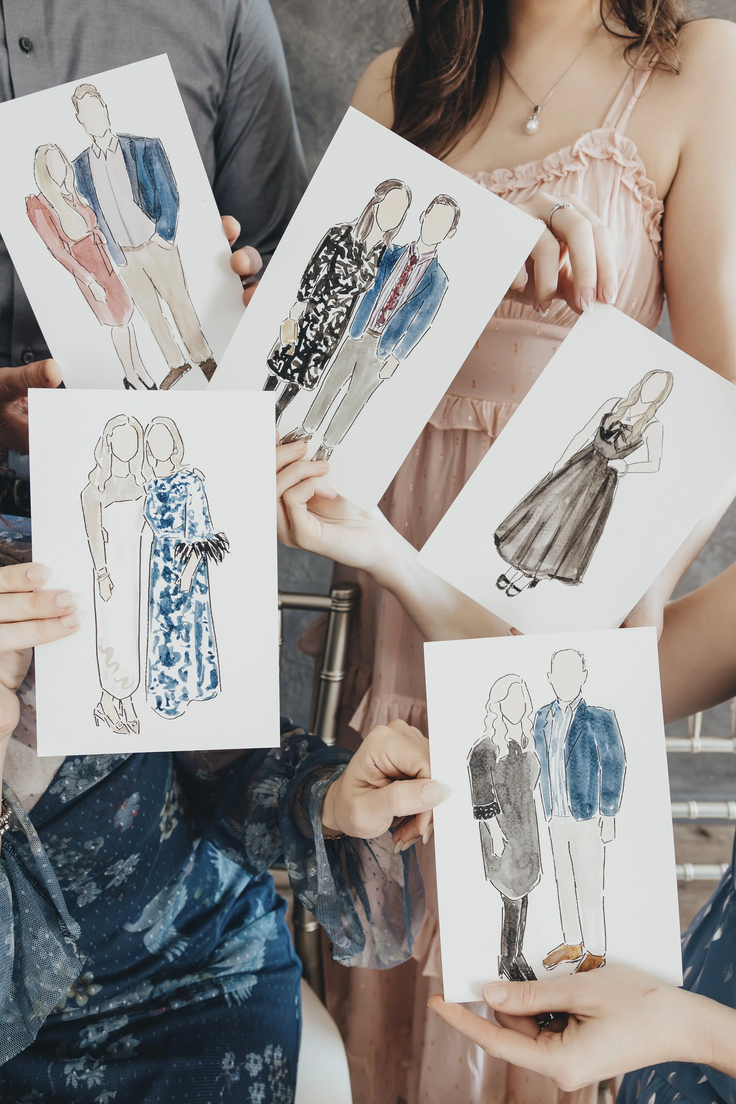 Artists holding up fashion sketches of various outfits at an event.