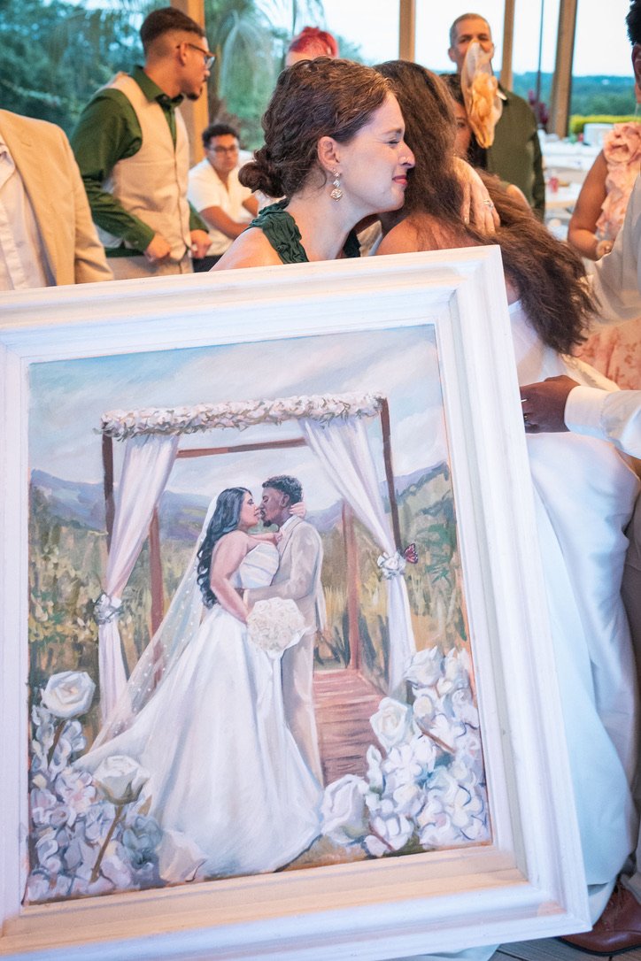 A painting of a newlywed couple kissing under a flower-draped canopy backdrop, surrounded by white roses.