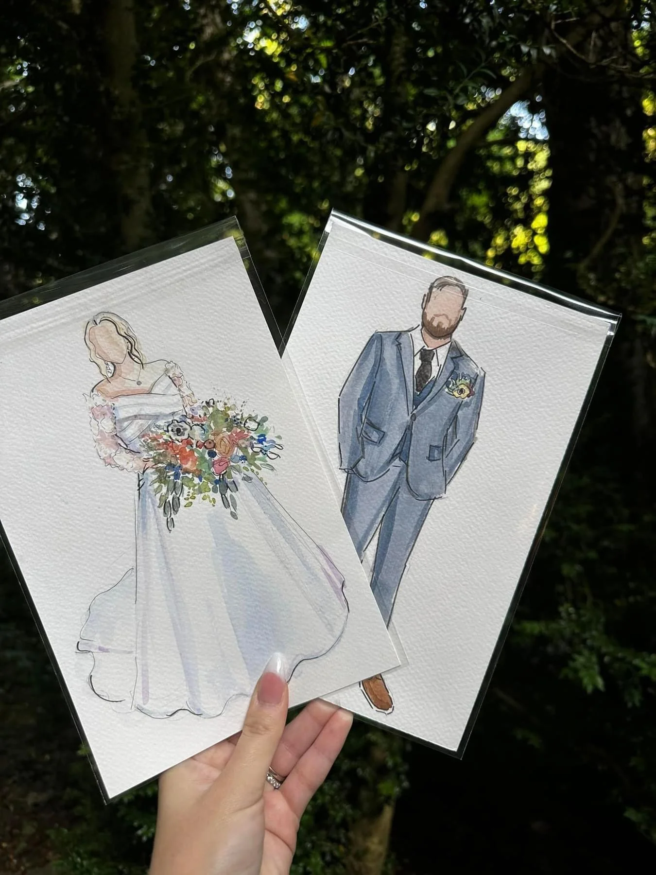 Watercolor illustrations of a woman in a wedding dress holding a large bouquet and a man in a suit with a boutonniere, held in front of a background of trees.