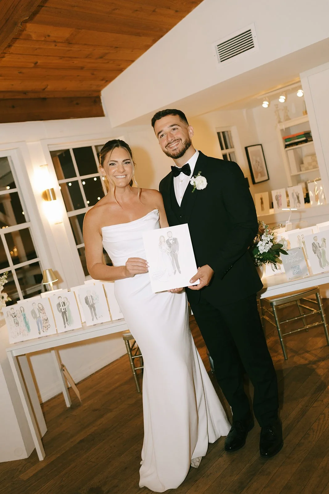 A bride and groom in wedding attire holding a portrait at their wedding reception.