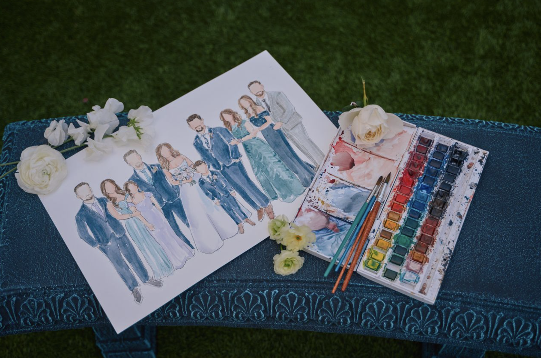 Watercolor wedding portrait of a bride, groom, and wedding party with flowers and watercolor paints on a table.