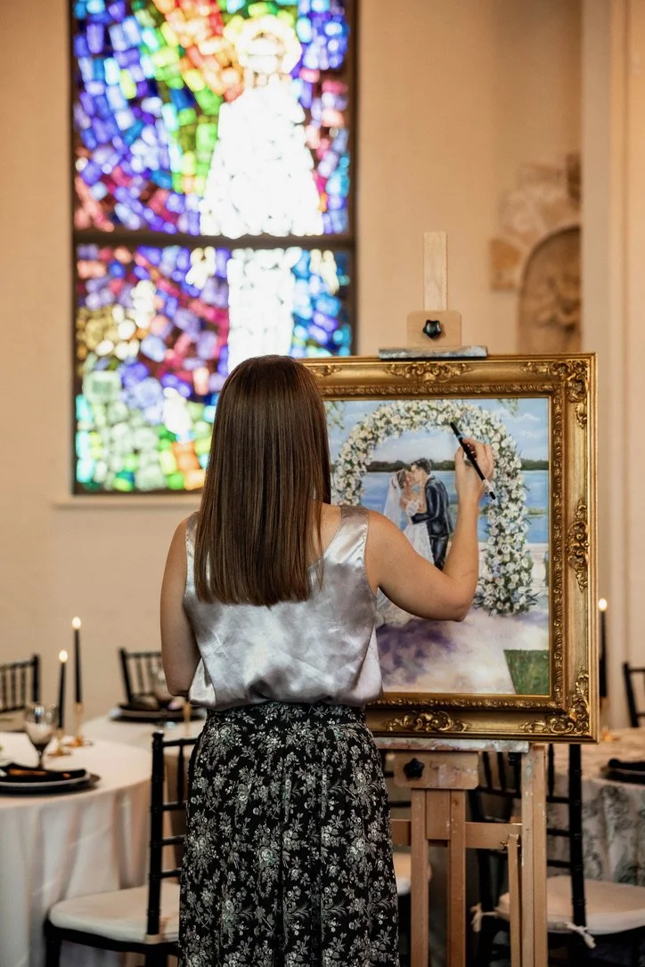 Brittany painting a wedding scene on a large framed canvas inside a church with stained glass windows.