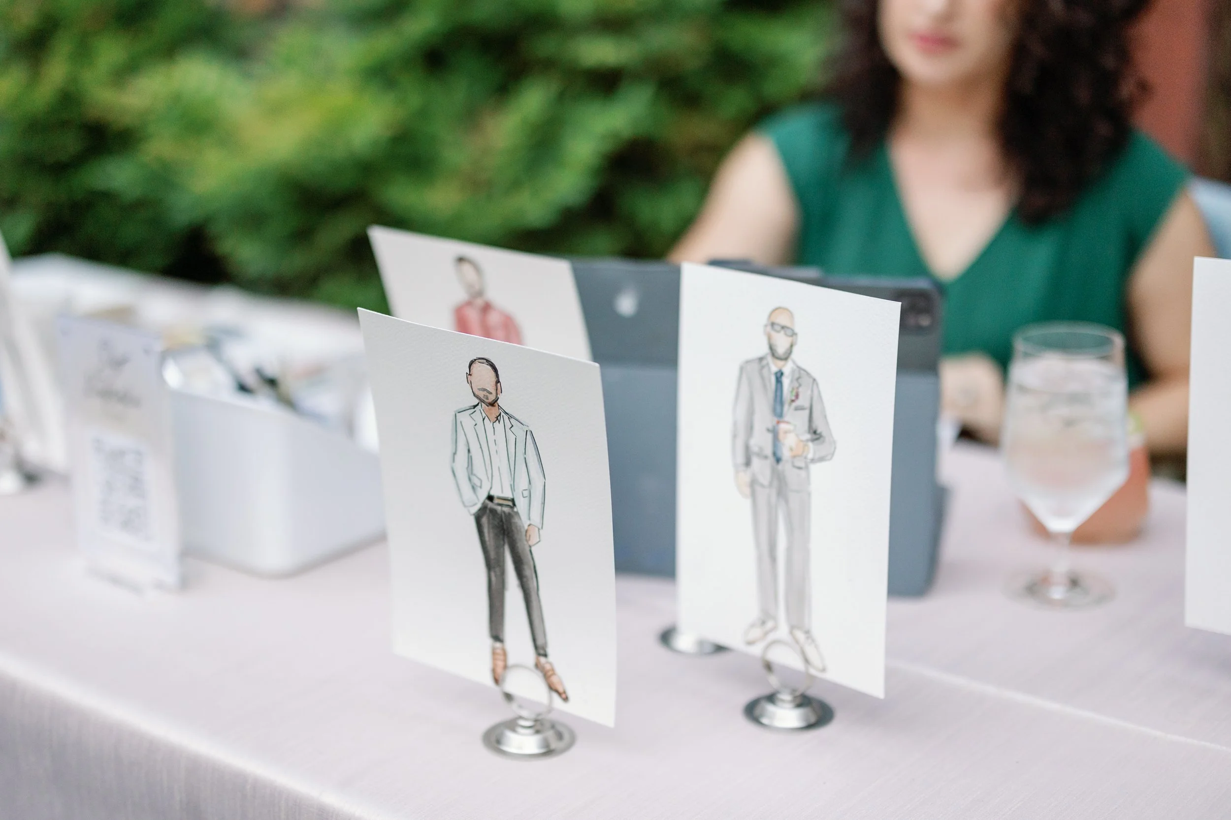 Table with illustrated guest portraits at outdoor event.