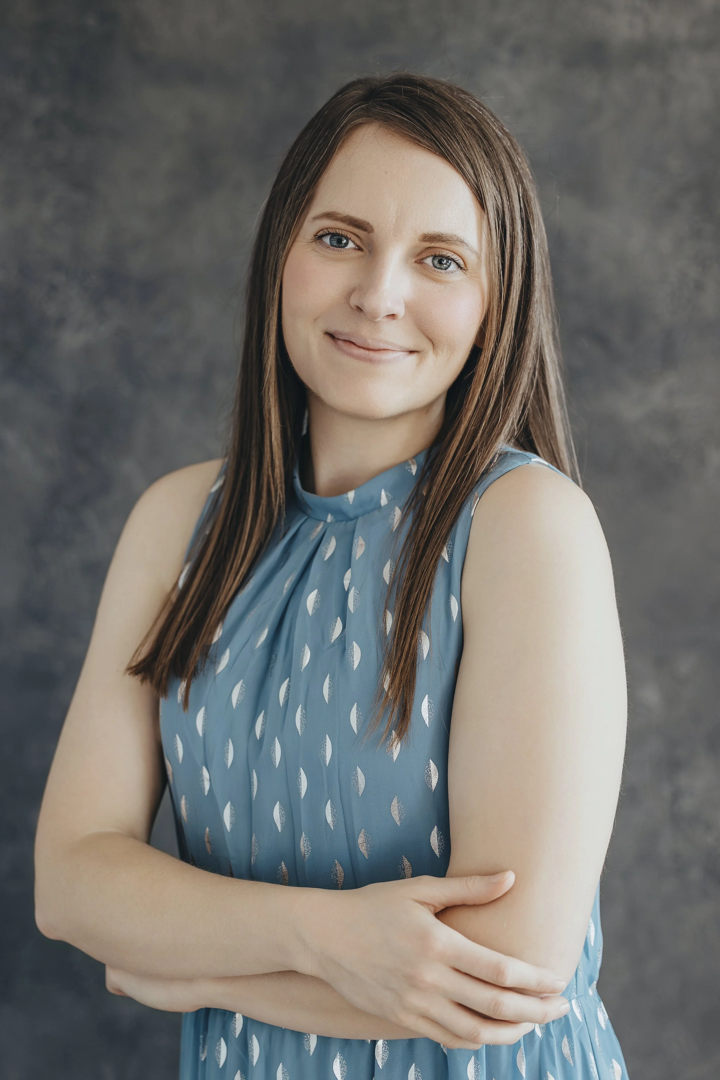 Brittany smiling with her arms crossed in front of a dark, textured background.