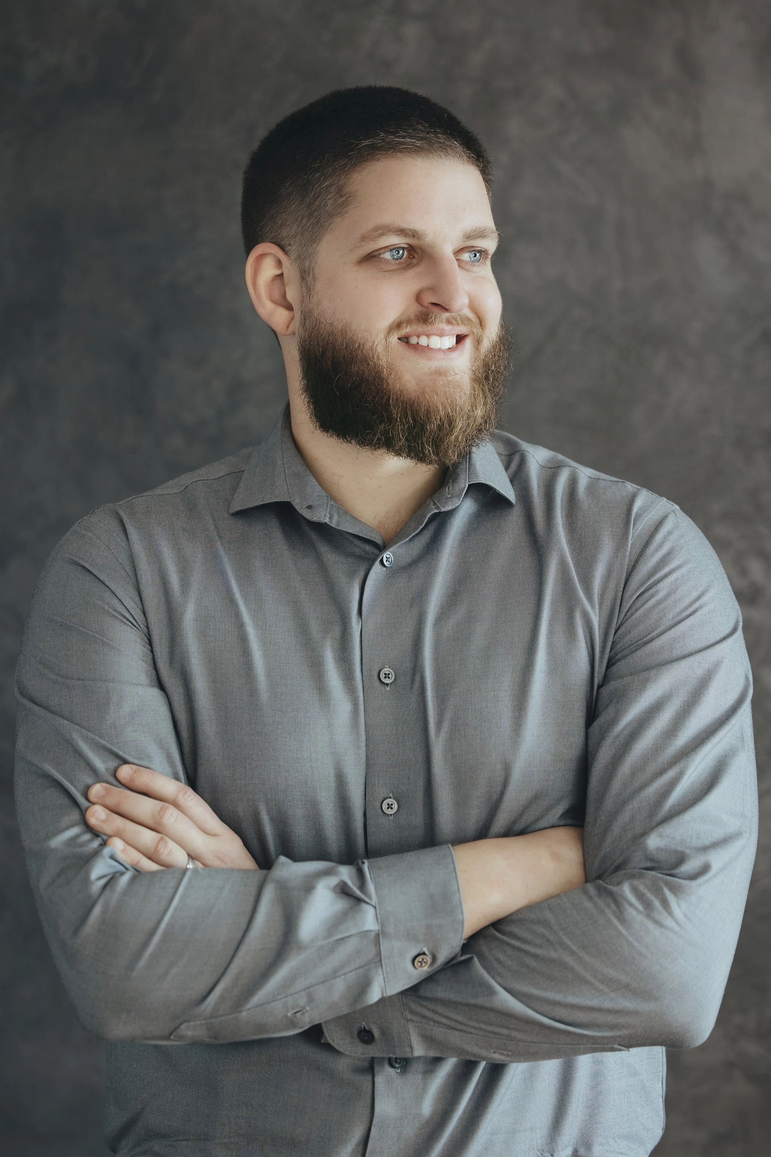 Caleb smiling and looking off to the side with arms crossed in front of a dark textured background.