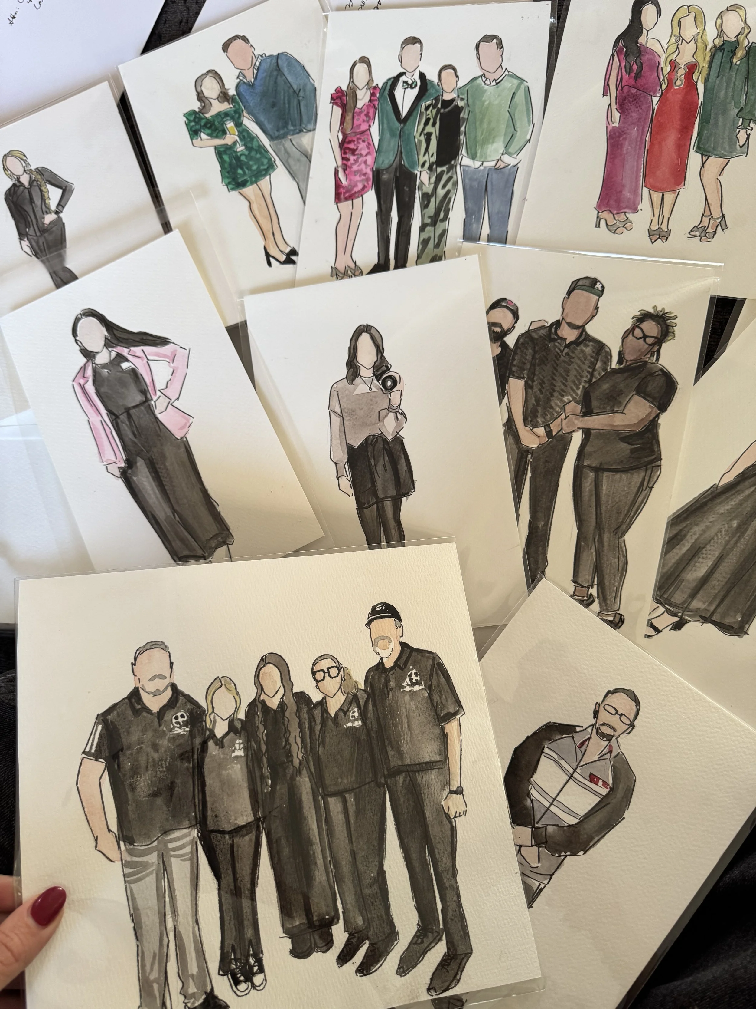 Collection of artistic illustrations of people, including groups and individuals, in various outfits displayed on a table.