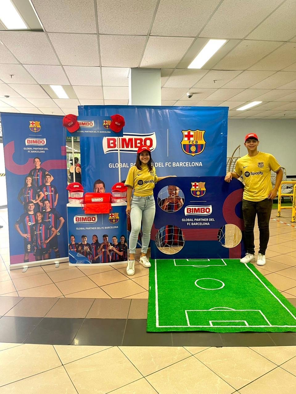 ChatGPT said:
Dos jóvenes frente a un display promocional del FC Barcelona, con gorras y camisetas, una pequeña cancha de fútbol artificial en el suelo, y banners con jugadores y patrocinadores del club. Activación organizada por Marketing Experience