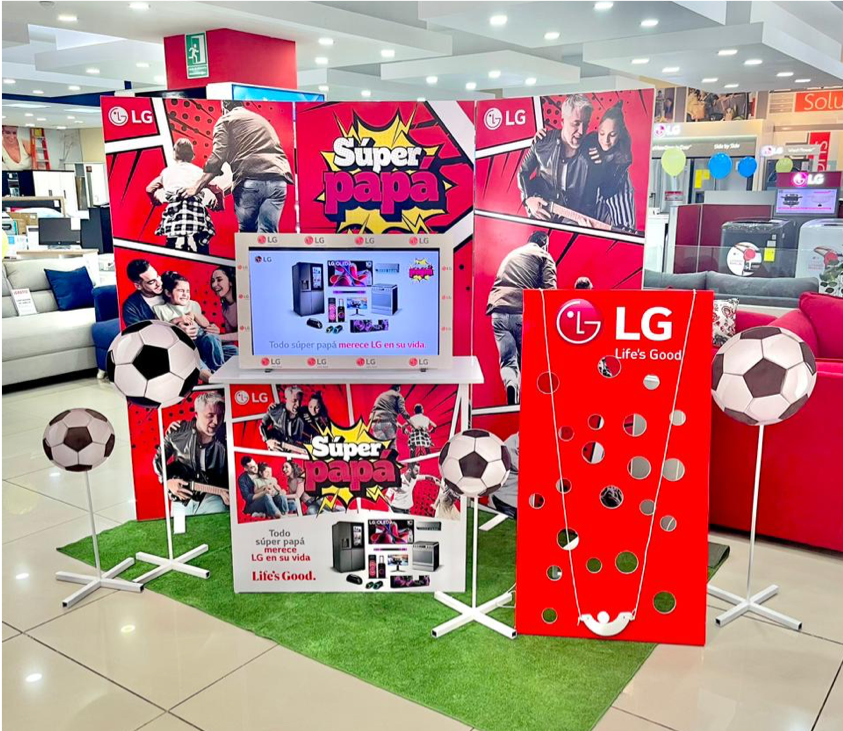 Display promocional de LG con la campaña Super Papá, mostrando imágenes de familias, niños y jóvenes, decorado con balones de fútbol y fondo rojo con logos de LG, ubicado en una tienda de electrónicos. Activación organizada por Marketing Experience.