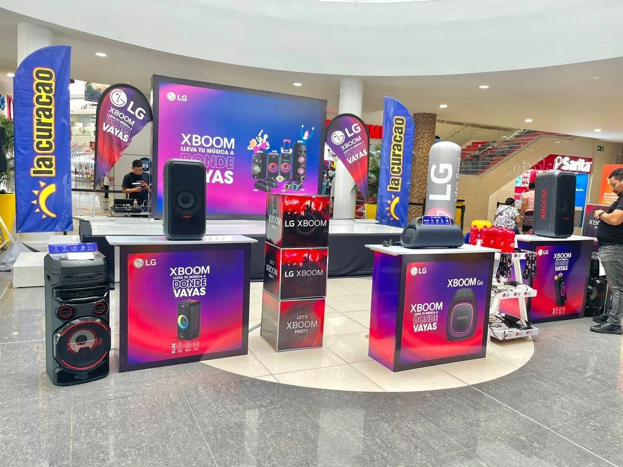 Stand electrónico en centro comercial promocionando los productos de audio LG XBOOM, incluyendo bocinas y subwoofers, con rótulos coloridos y banners promocionales. Activación organizada por Marketing Experience.