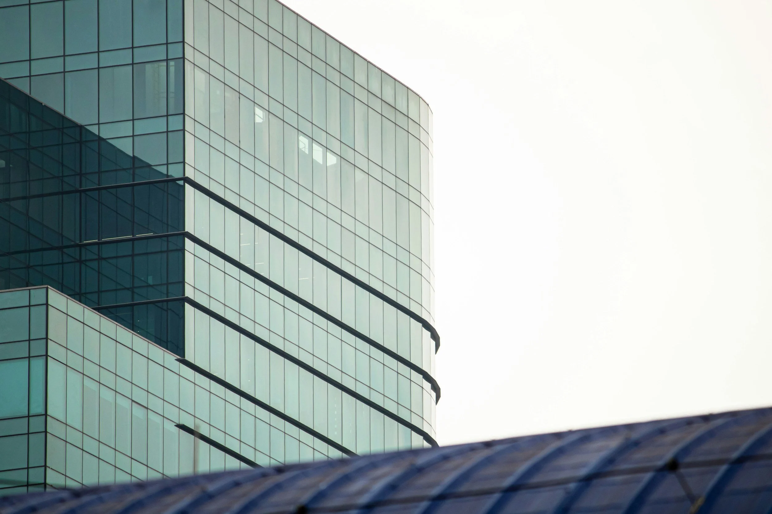 Close-up of a modern glass office building with reflective windows, against a bright sky, with a curved glass structure in the foreground. Clean windows from a window cleaner. Commercially cleaned space. clean business area.