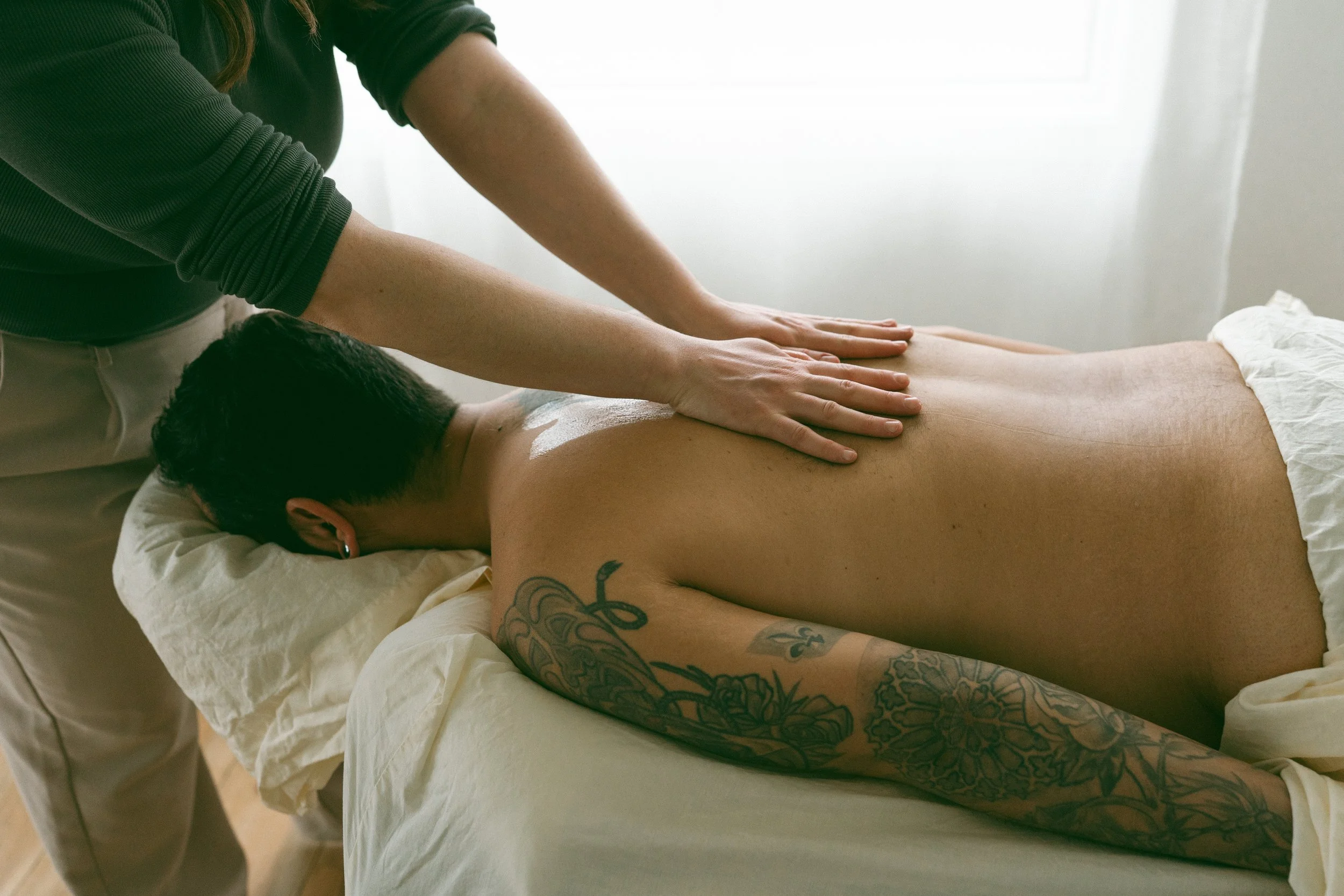 A person receiving a back massage while lying face down on a massage table, with Emma, a registered massage therapist applying pressure with their hands.