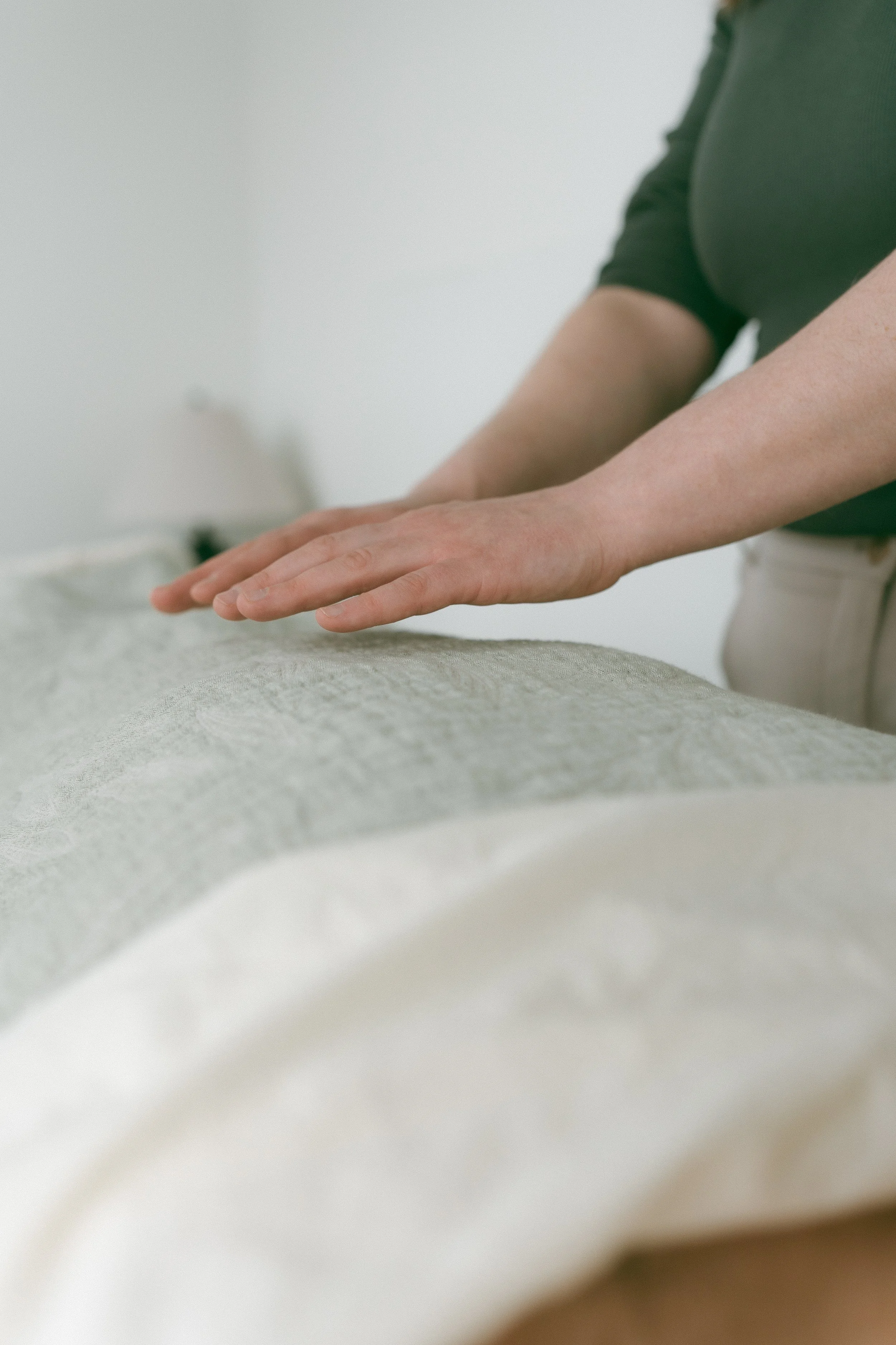Close-up of a person’s hands performing a massage or physical therapy, with a focus on the hands and forearms, on a soft surface.