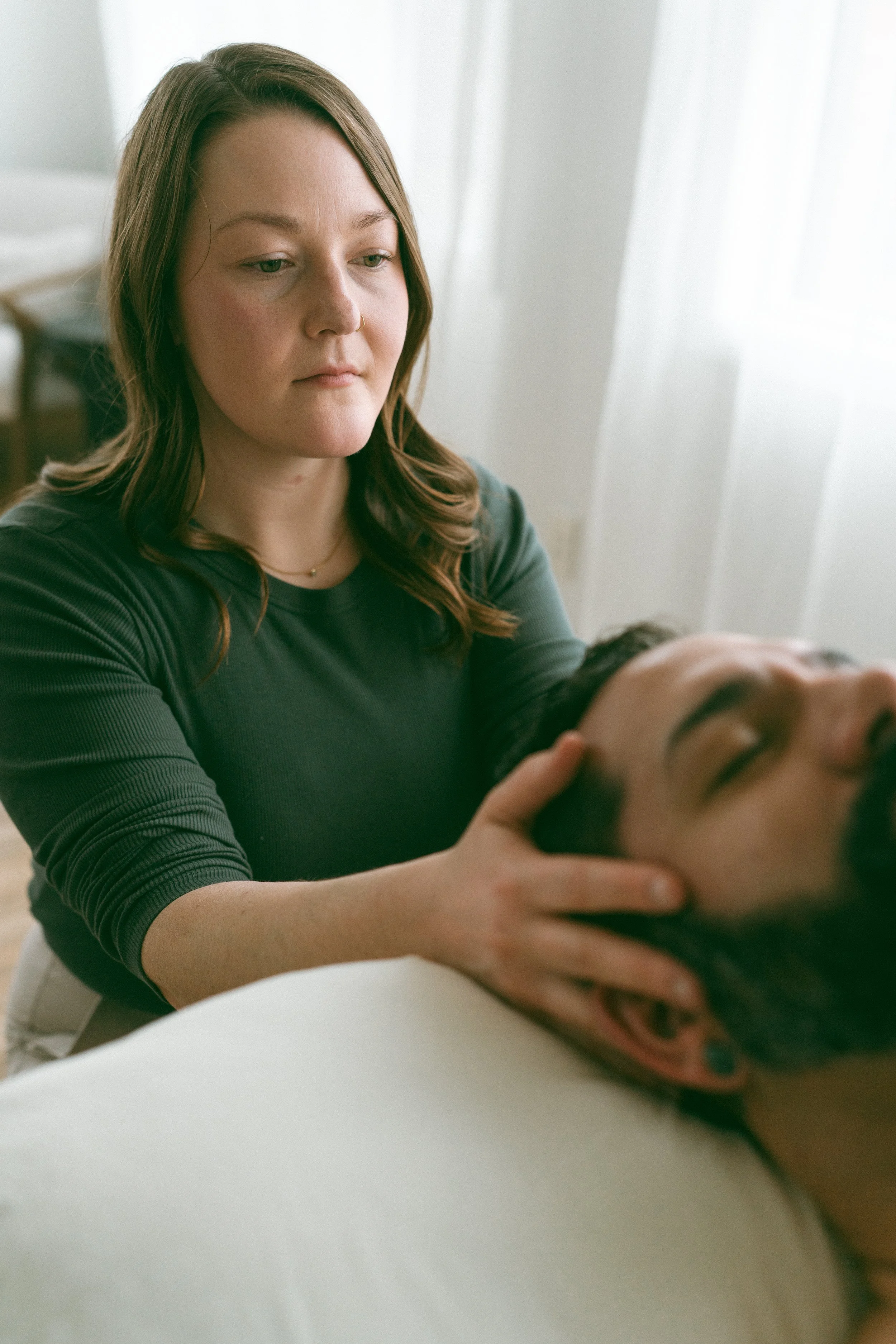 Emma providing an Access Bars session to a man lying down with his eyes closed.