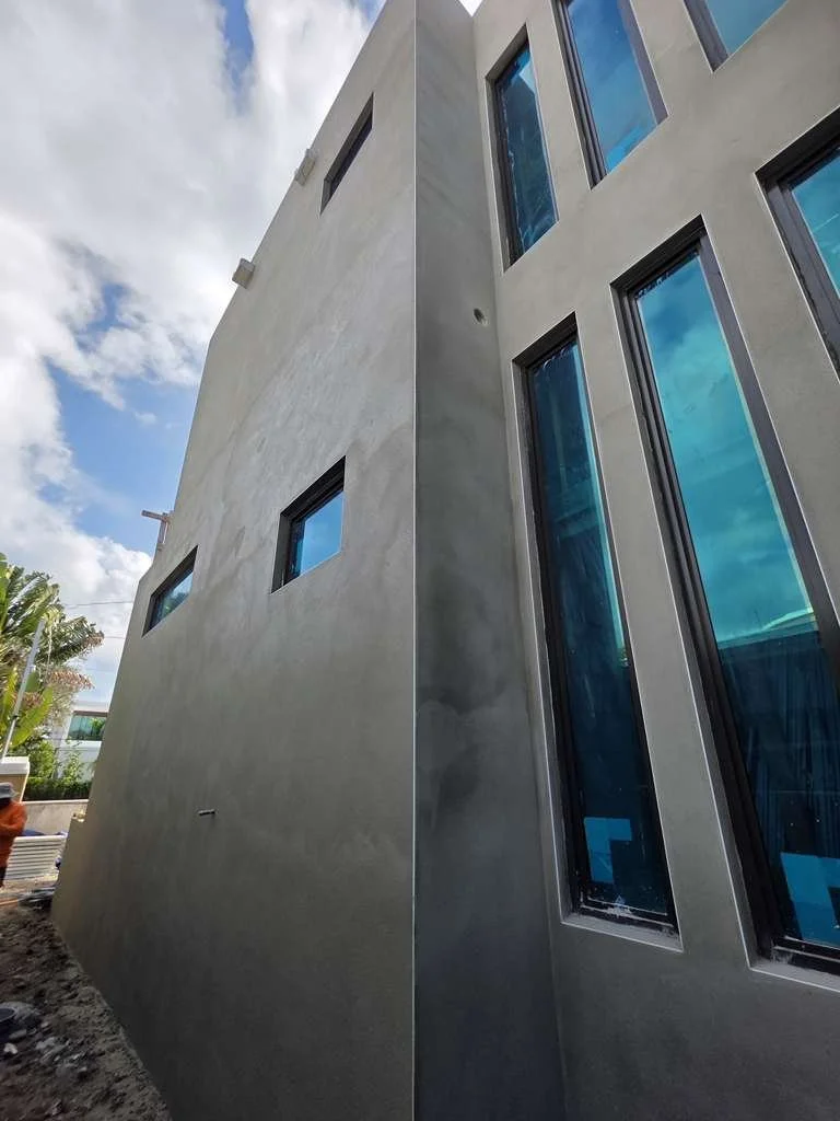 Close-up of a modern residential building with beige, light gray, and dark gray exterior walls, and small windows, against a gray sky.