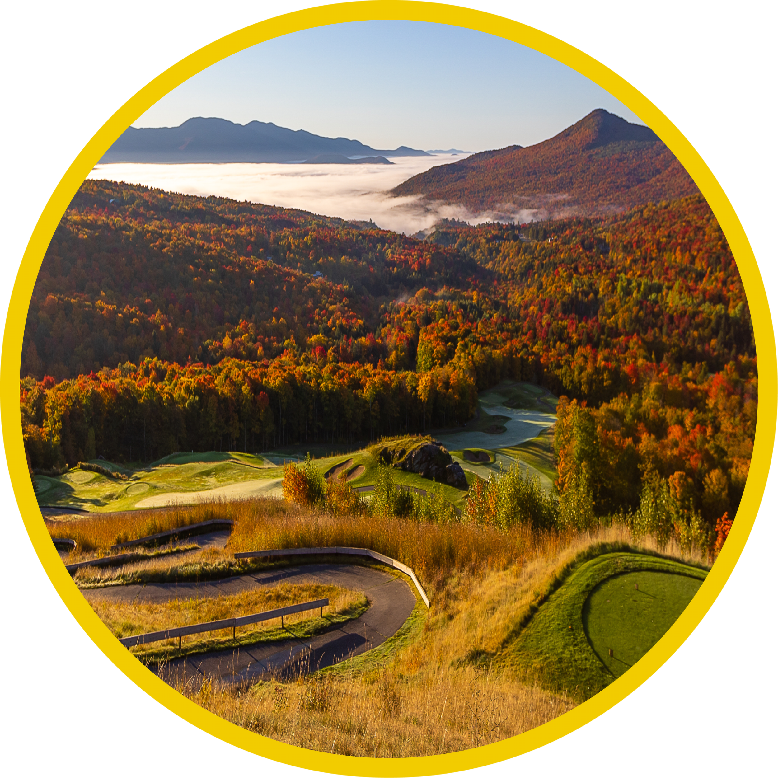 A scenic view of a golf course surrounded by autumn trees, with mountains in the background and a field of fog or low clouds in the distance.