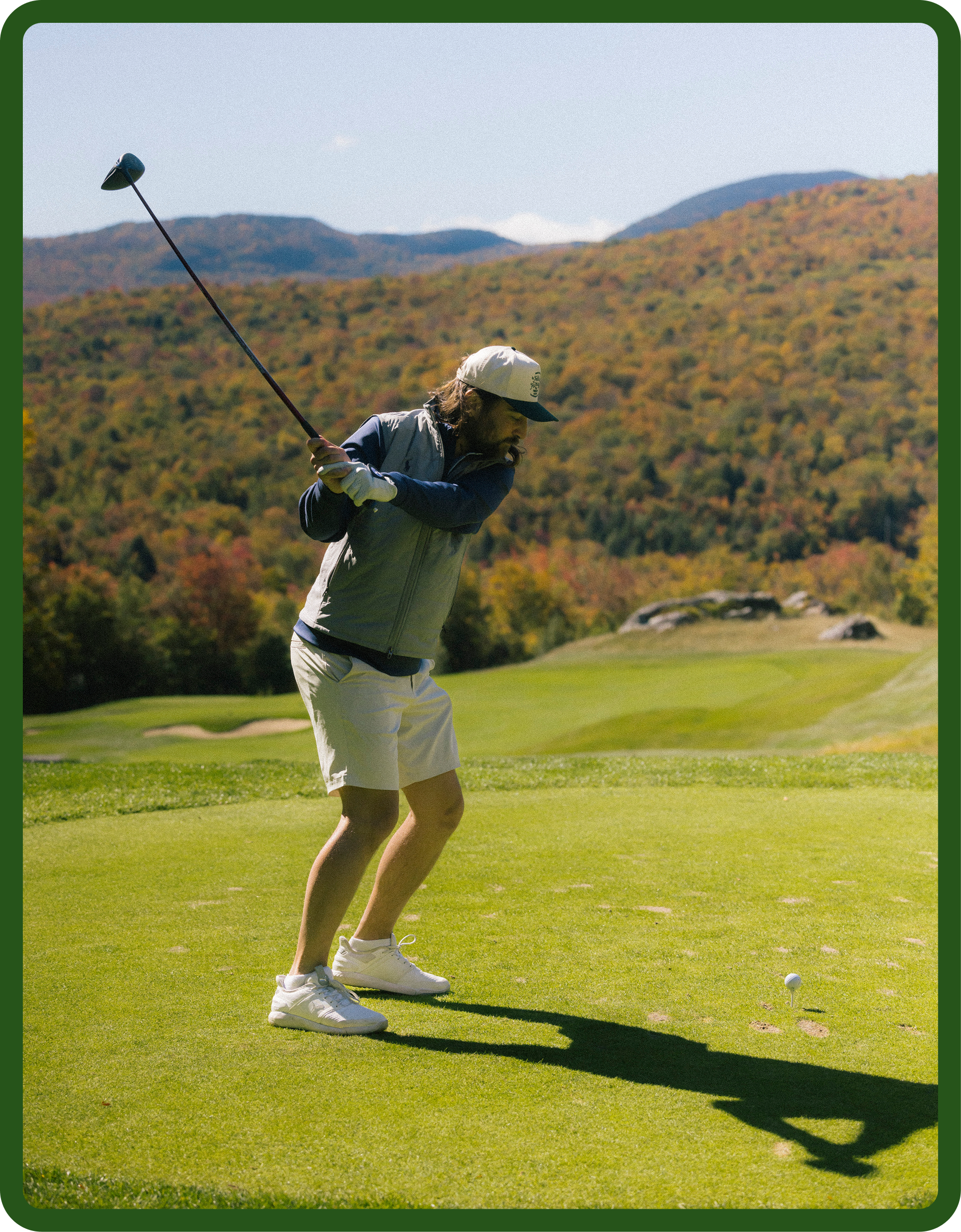A man playing golf on a course with hills and trees in the background during daytime.