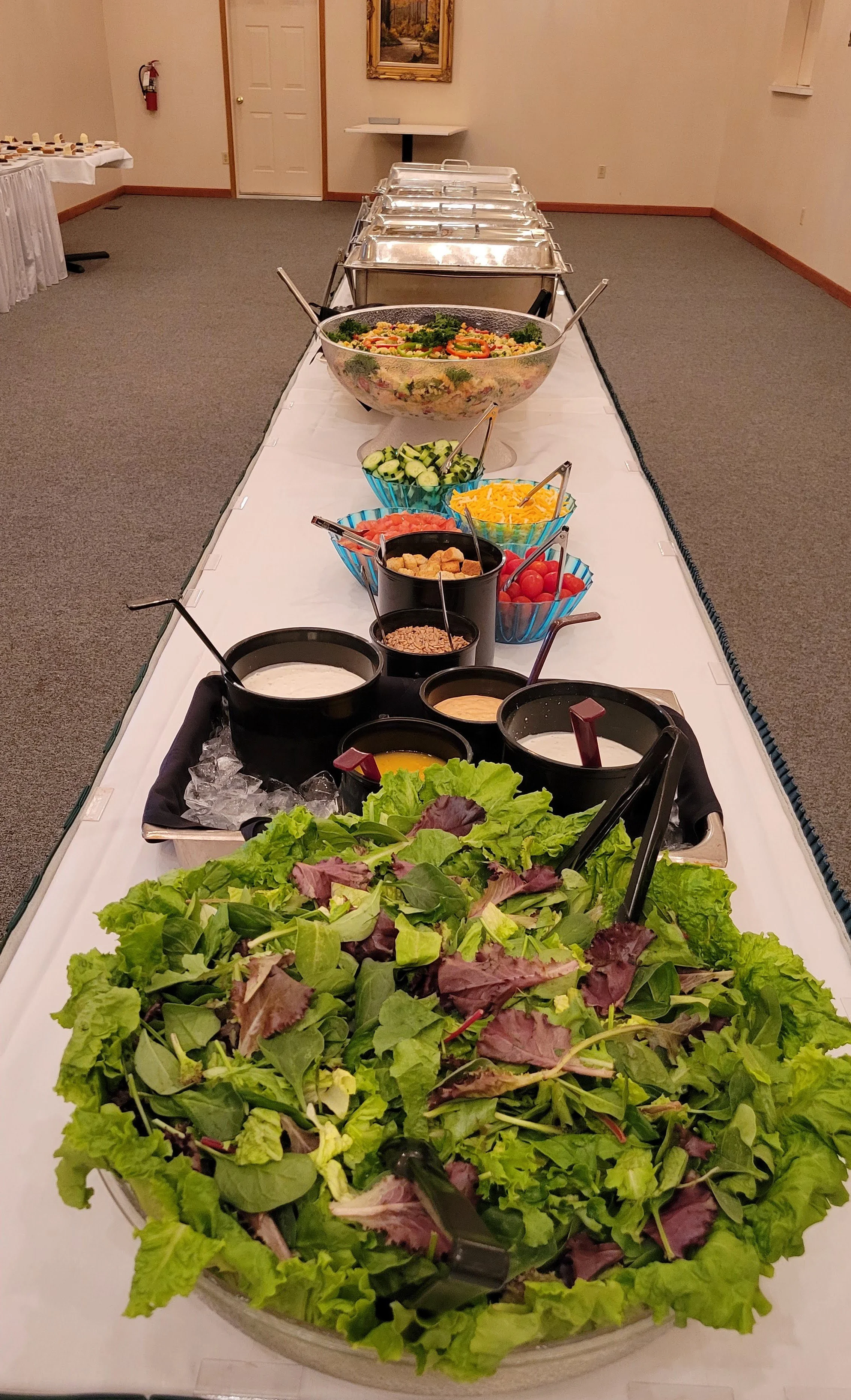 Buffet table with assorted salads, vegetables, and dressings in a banquet room.