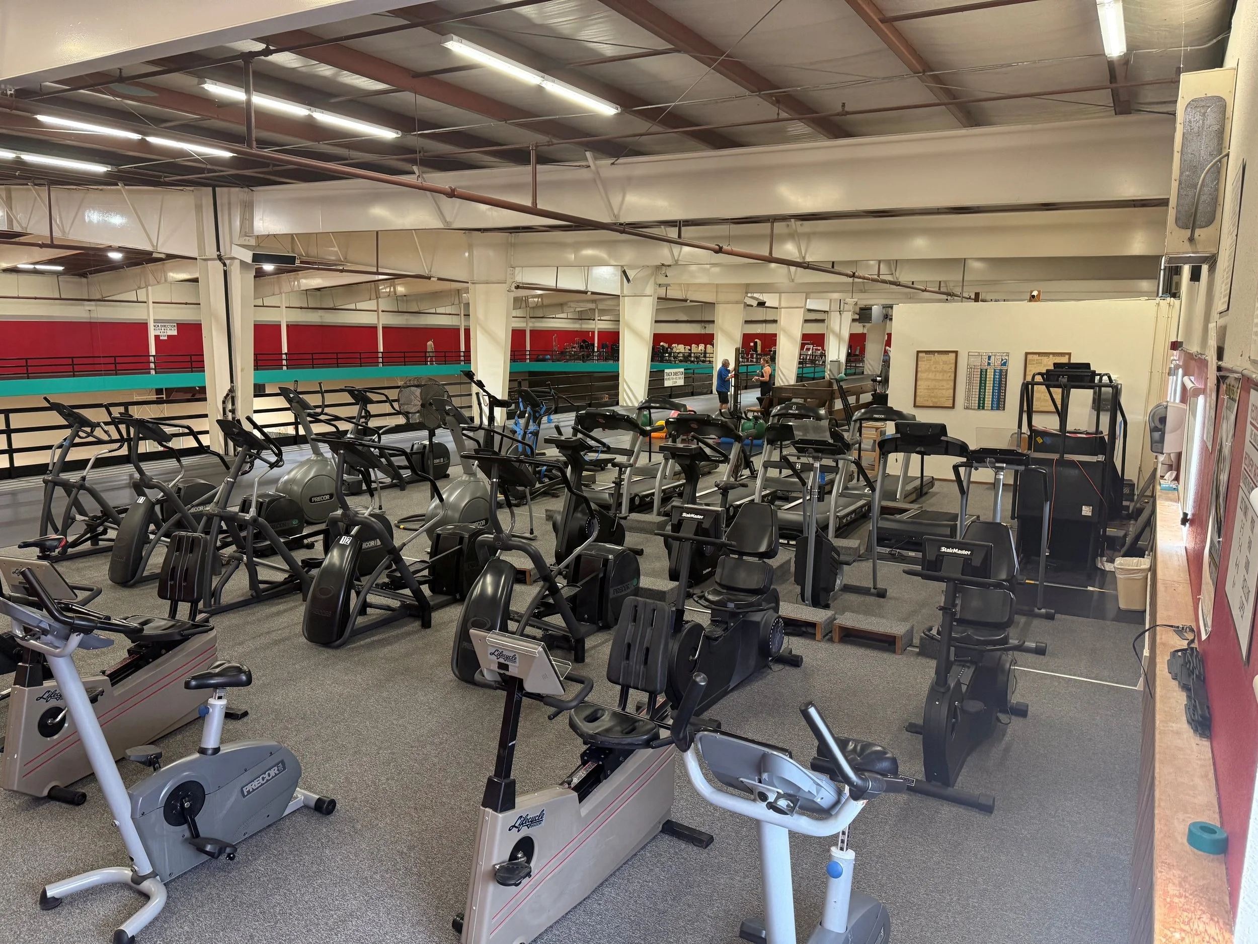 An indoor gym with various exercise equipment including treadmills, ellipticals, and stationary bikes. 