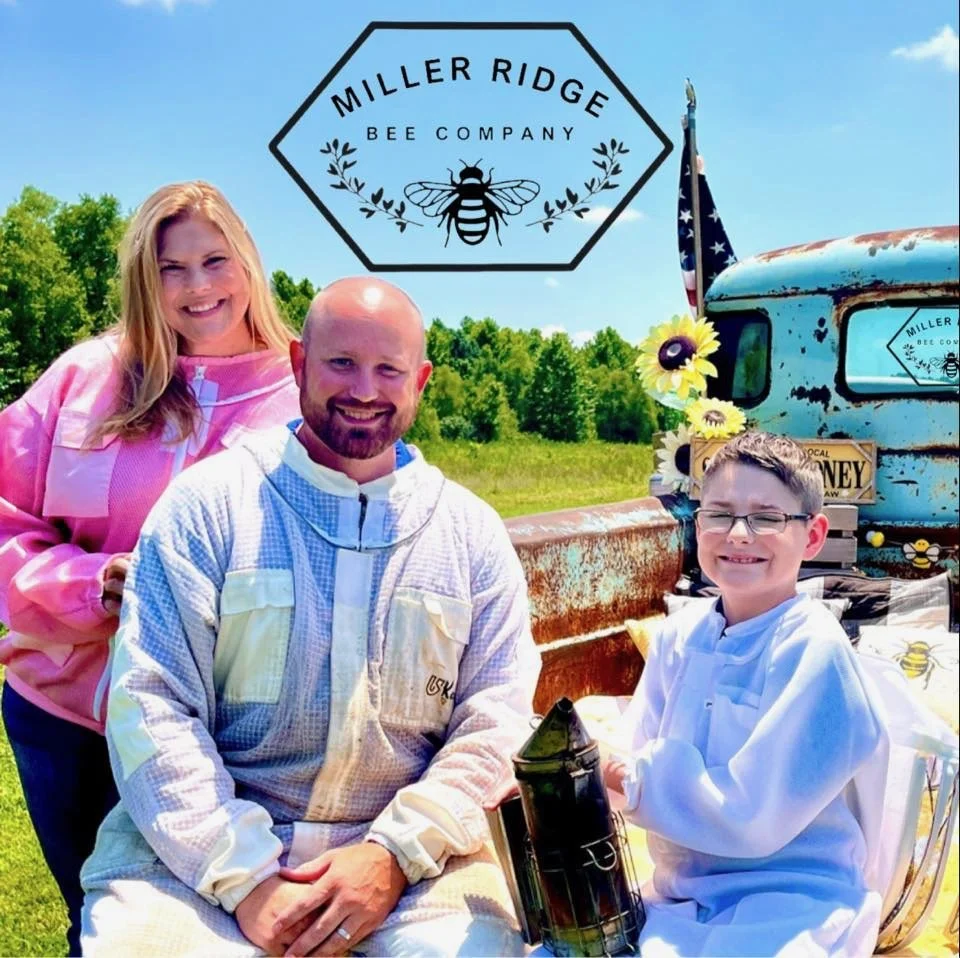 Chelsea, Erik, and Camden, outside in front of a blue rusty truck decorated with sunflowers, a sign reading 'Miller Ridge Bee Company', and an American flag. The group is smiling, and Camden is holding a beekeeping smoker.