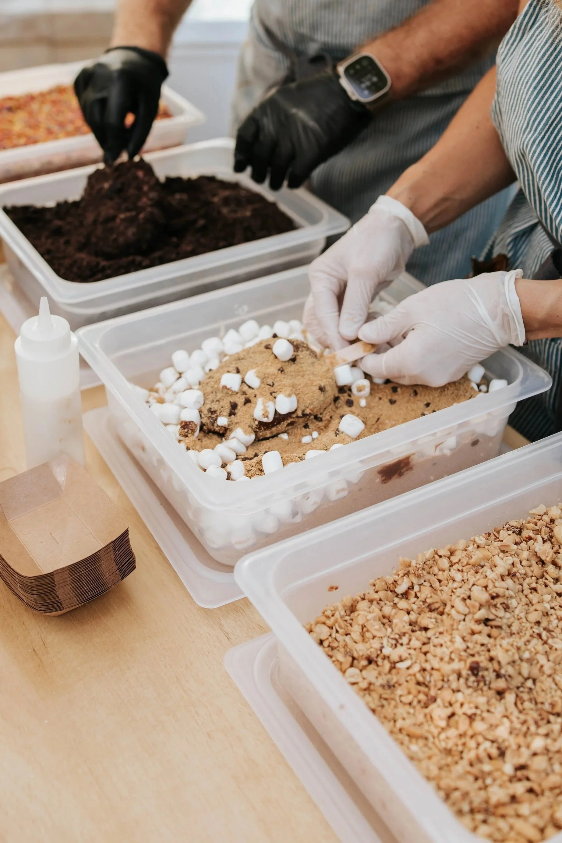 A person dipping a chocolate dipped icecream in graham cracker and mini marshmallow