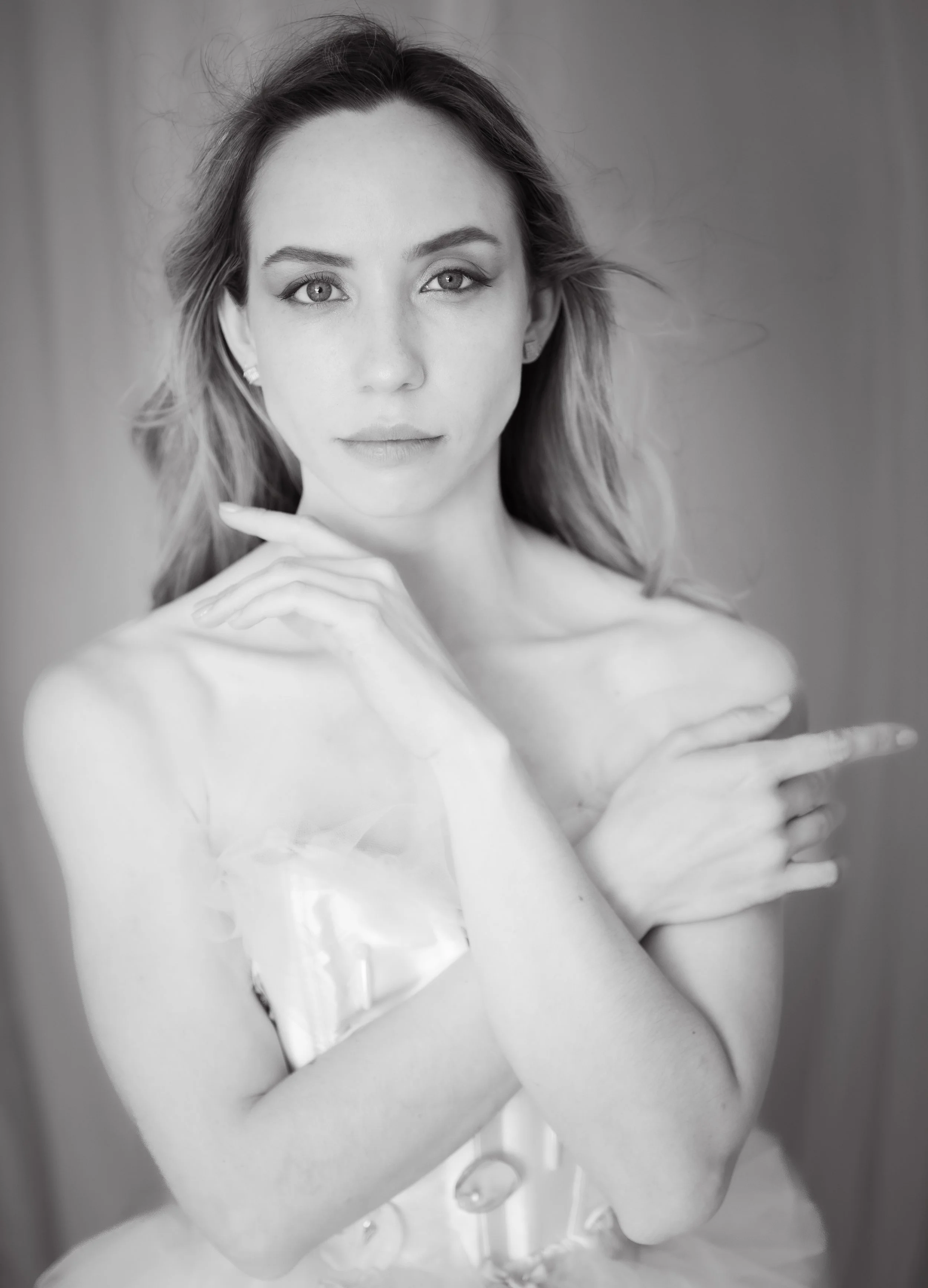 Black and white portrait of a young woman with light-colored hair, looking directly at the camera, with her hands crossed over her shoulders.