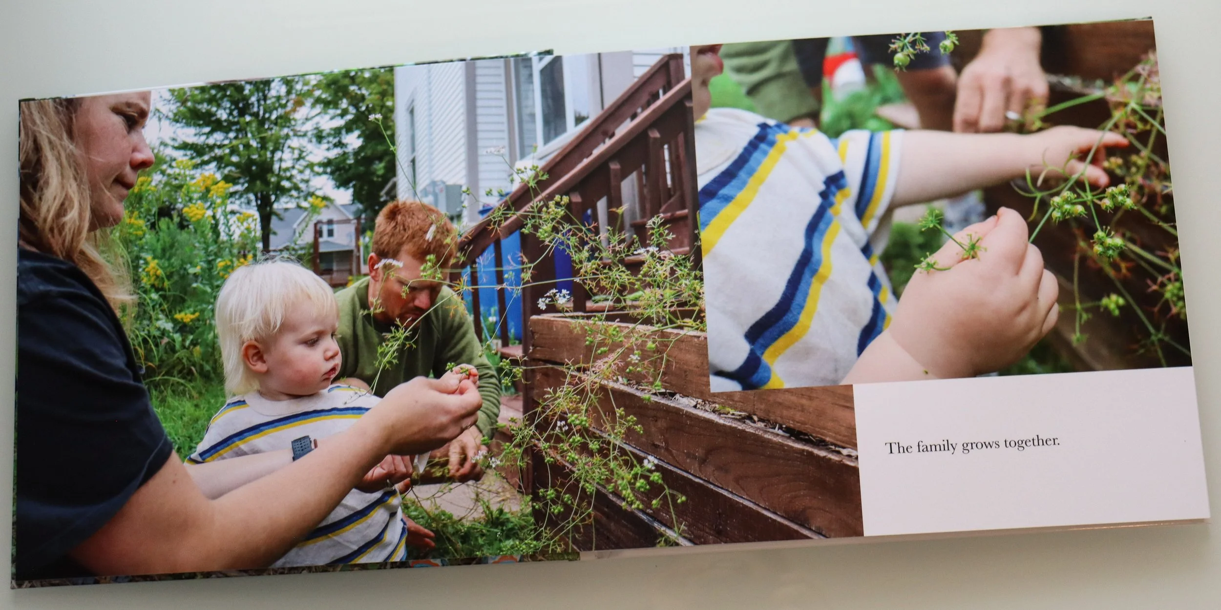 A family of three, a woman, a man, and a young child, gardening outdoors, the woman and child are close to the camera, with the woman helping the child pick a berry from a plant. The background shows other plants and a wooden staircase.
