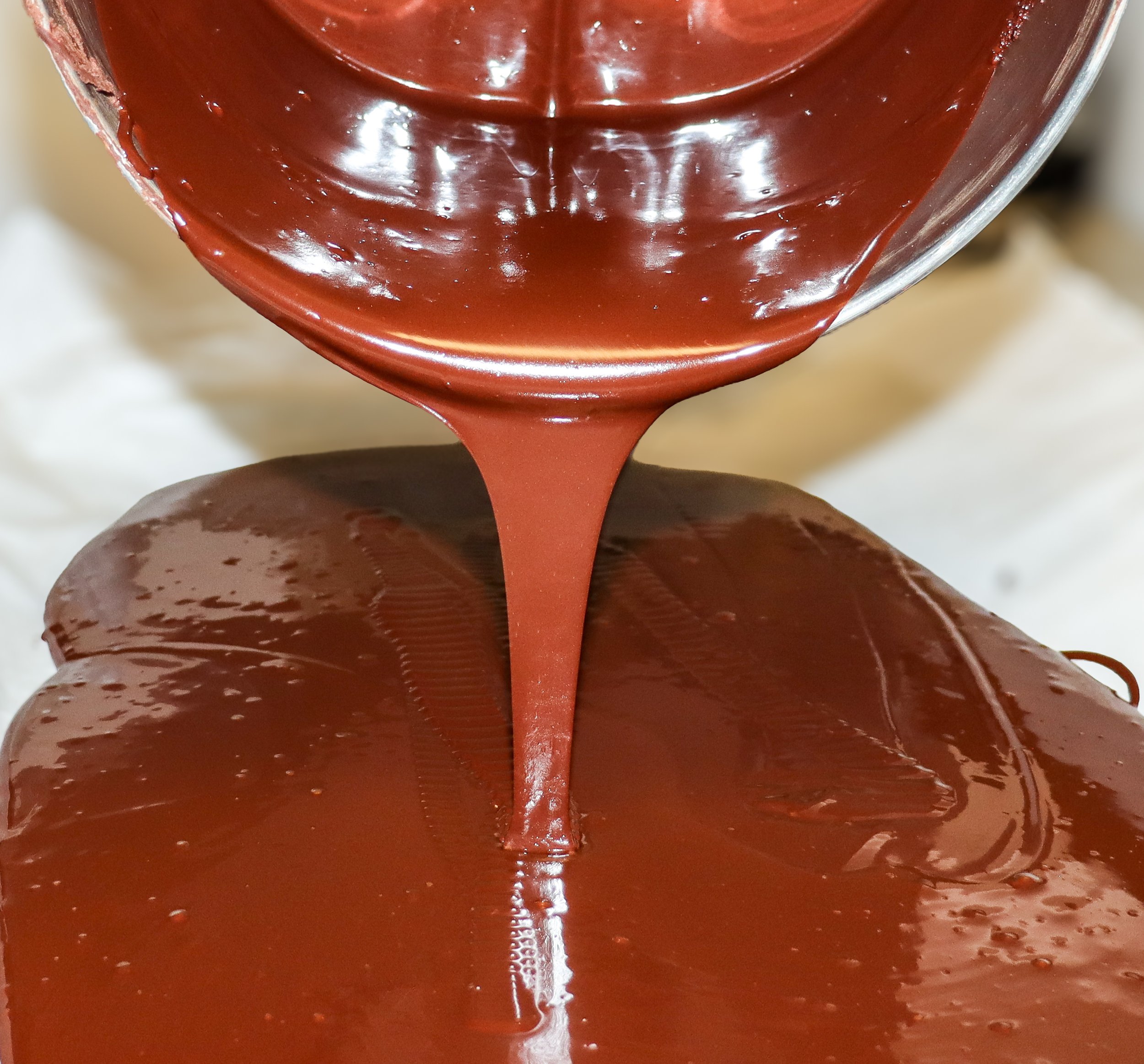 Hot melted chocolate being poured, forming a smooth, shiny surface with a rich, dark brown color.