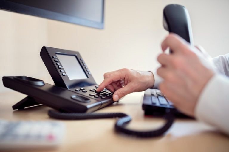 Person holding a landline phone receiver and pressing buttons on a desk phone in an office