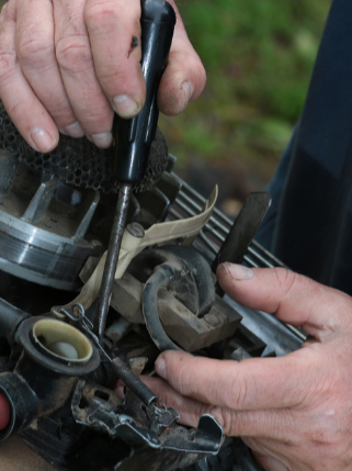 Close-up of a person's hands repairing a small engine or machine, using a screwdriver on a part of the equipment as services offered at Raeford Hardware.