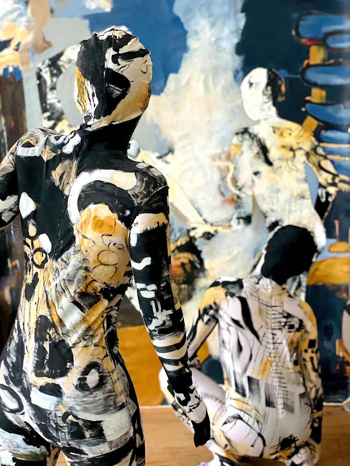 Abstract art sculptures of human figures with a mix of black, white, and beige paint patterns, displayed against a background of similar artworks.