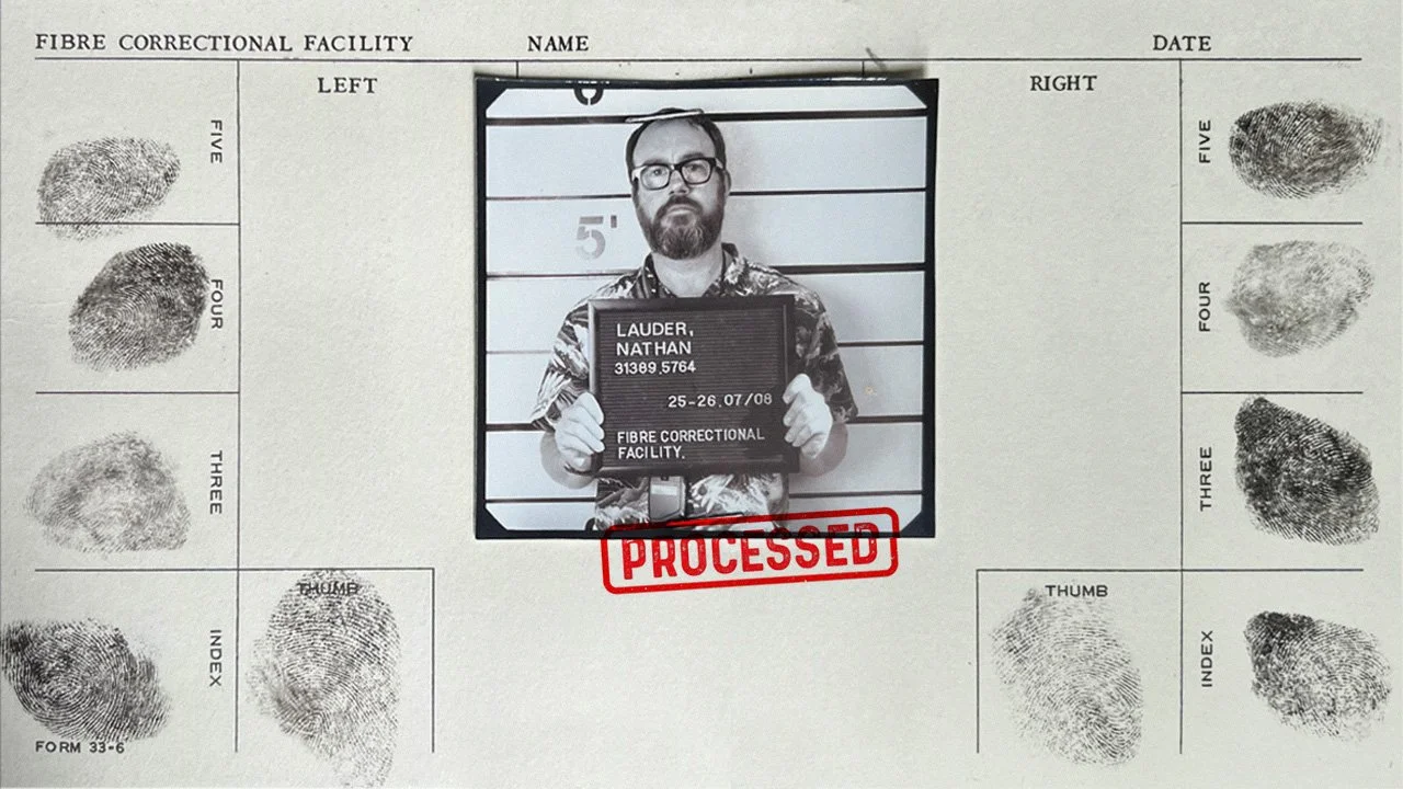 Mugshot of a man with glasses, holding a placard with the name Nathan Lauder, and date of birth, in front of a height chart, with finger and thumbprints on either side, on a processed fingerprint card.