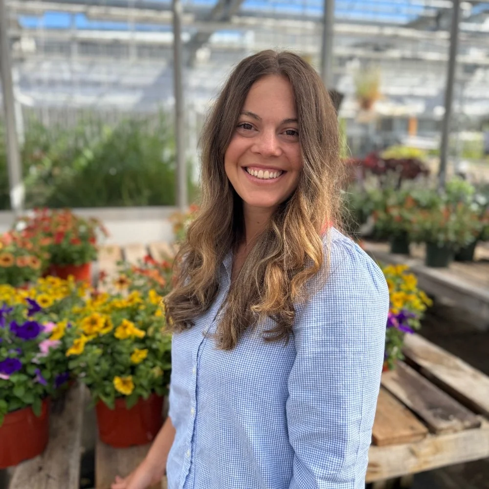 Abby Behar, Needham Massachusetts EMDR therapist and nurse; woman with long brown hair, smiling, wearing a white and blue patterned blouse and blue jeans, standing outdoors in front of green bushes and trees.