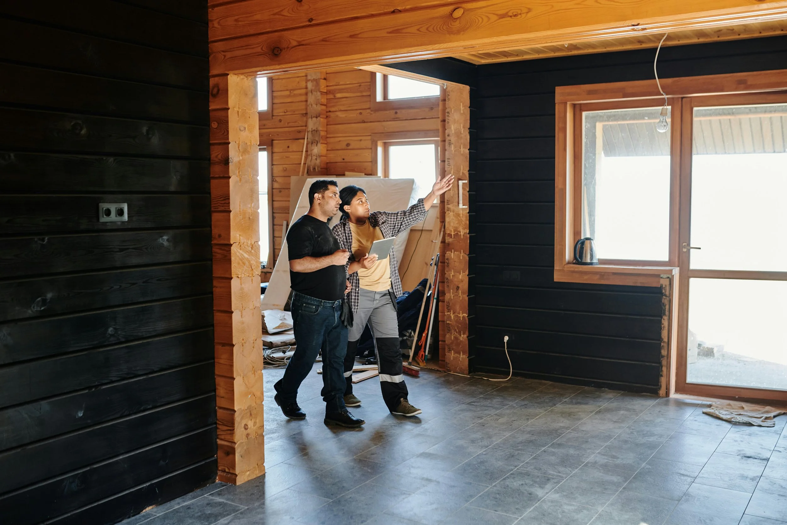 Two people inspecting the interior of a house under construction, with one person pointing towards the window and the other holding a tablet.