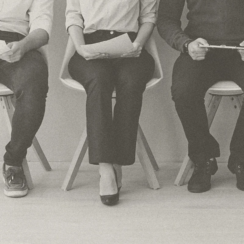 Three people sitting on chairs, holding papers or tablets, in a row.