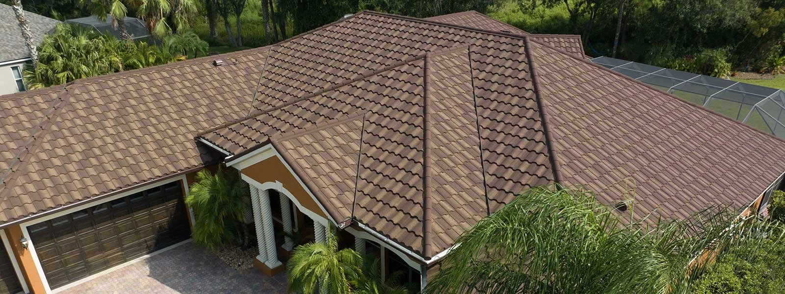 Aerial view of a house with a brown tiled roof, front porch with columns, and surrounded by green plants and trees.
