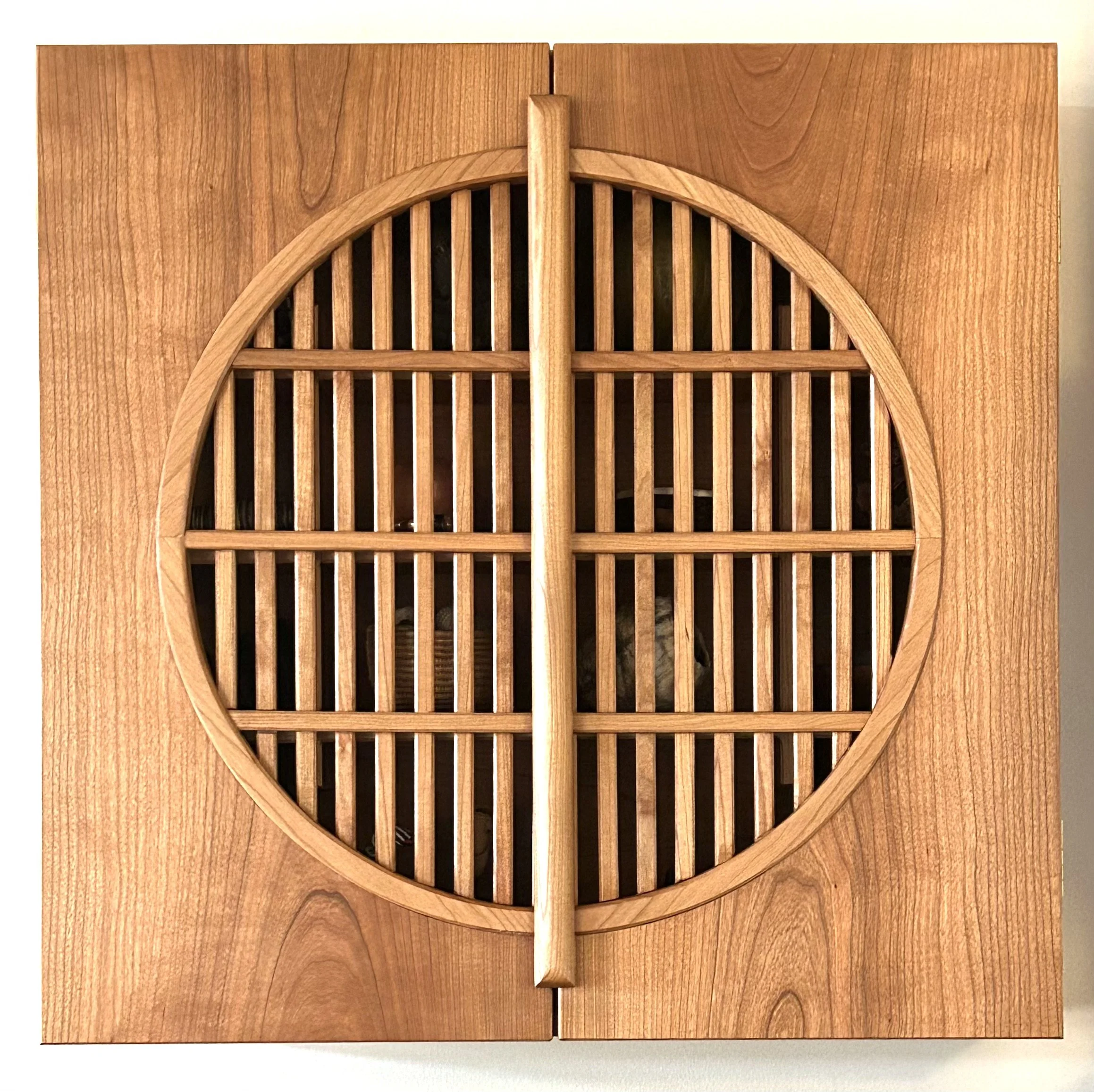 Wooden box with a circular vent with a carved, grid-like pattern and a central vertical divider.