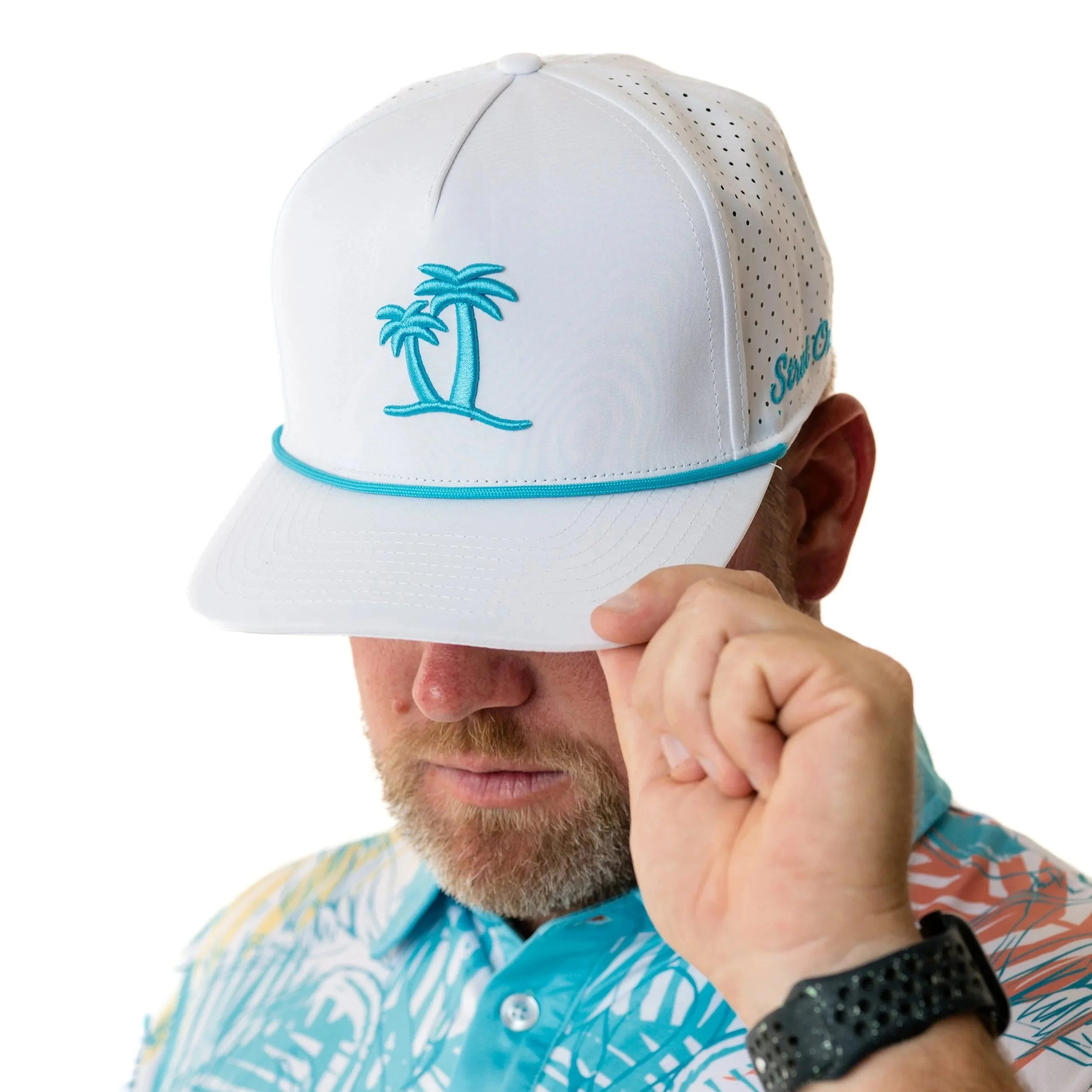 A man wearing a white golf cap with 'Sandcrane Golf' logo stands outdoors with a grassy area in the background.