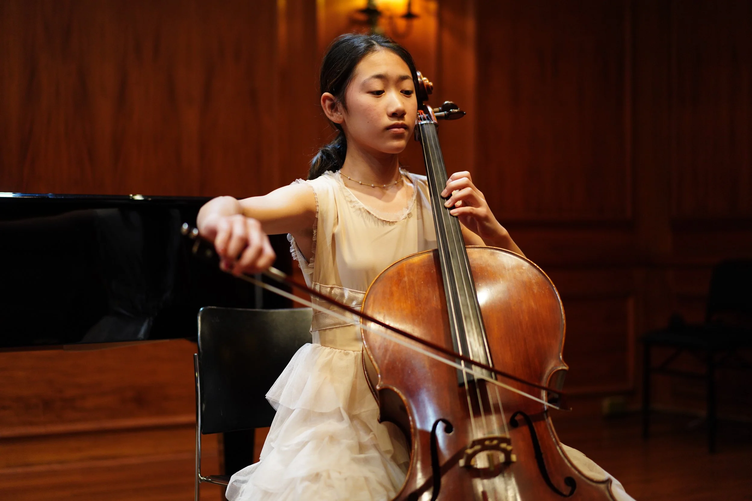 Young girl playing the cello during a concert in a wooden-paneled room.