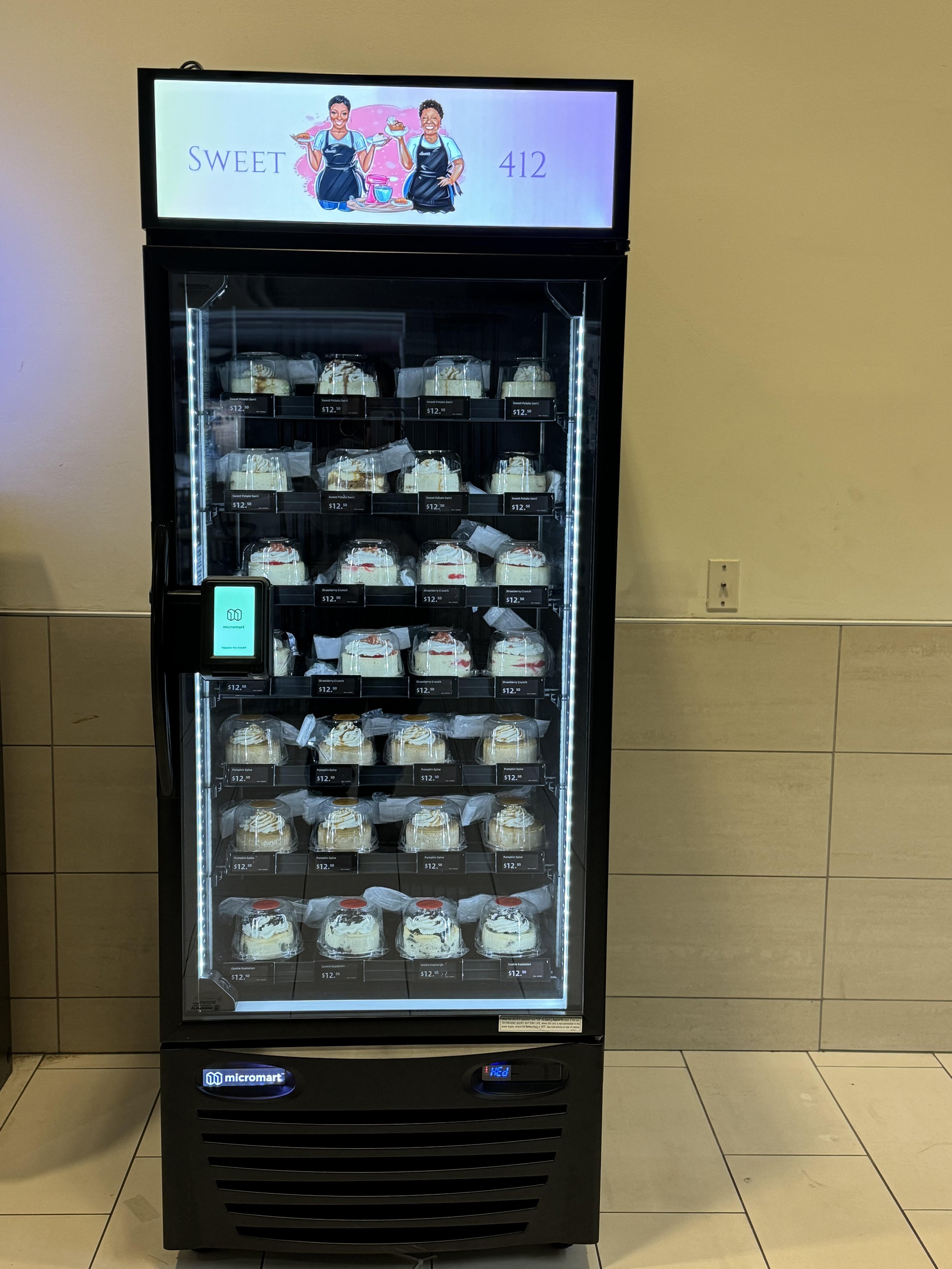 A vending machine with glass door stocked with cakes. The top of the machine has a sign with an illustration of two women holding cakes, labeled 'Sweet 412'.