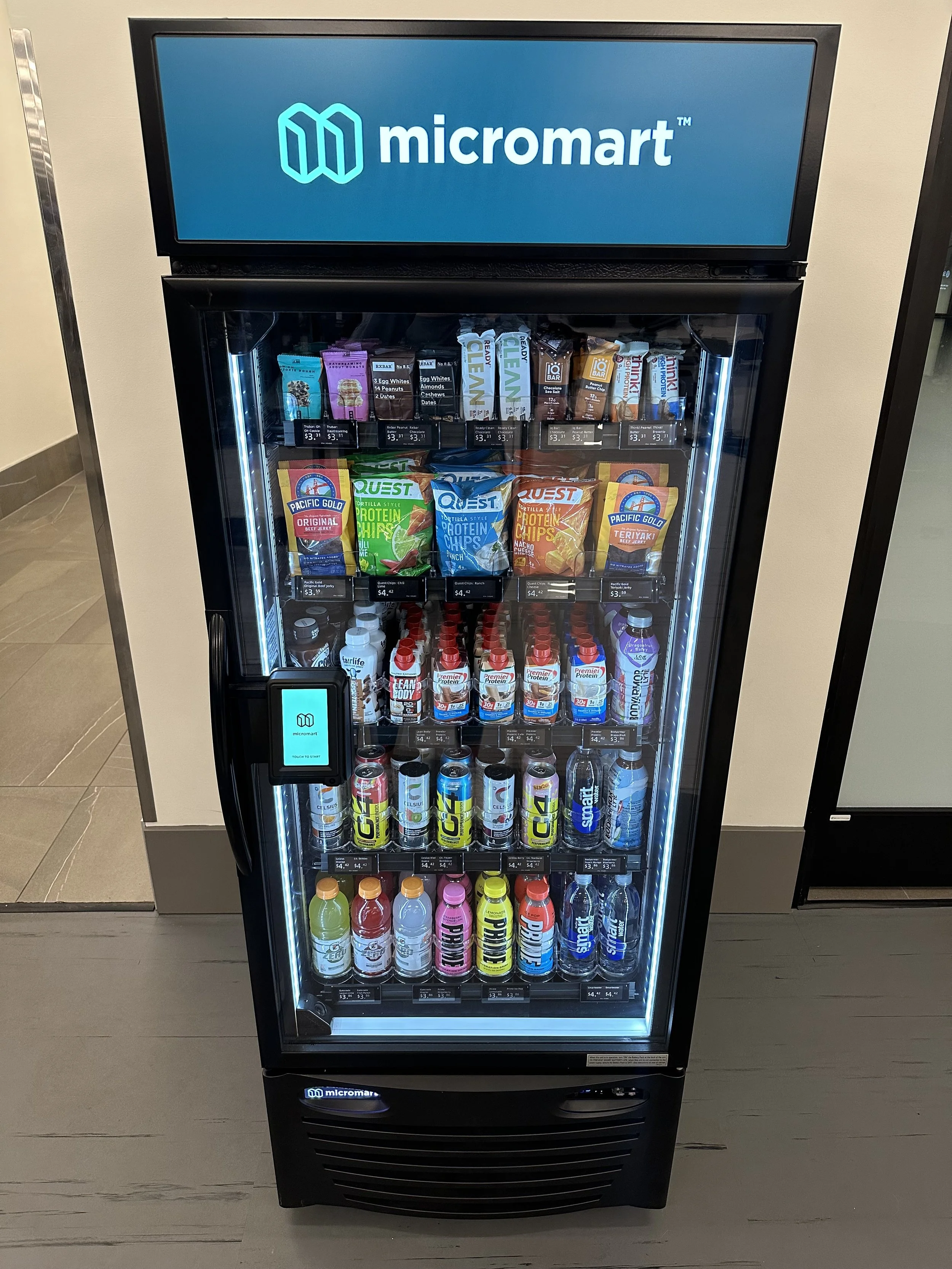Vending freezer with snacks and drinks displaying the Micromart logo on LED screen at the top and a smaller screen on the left side.