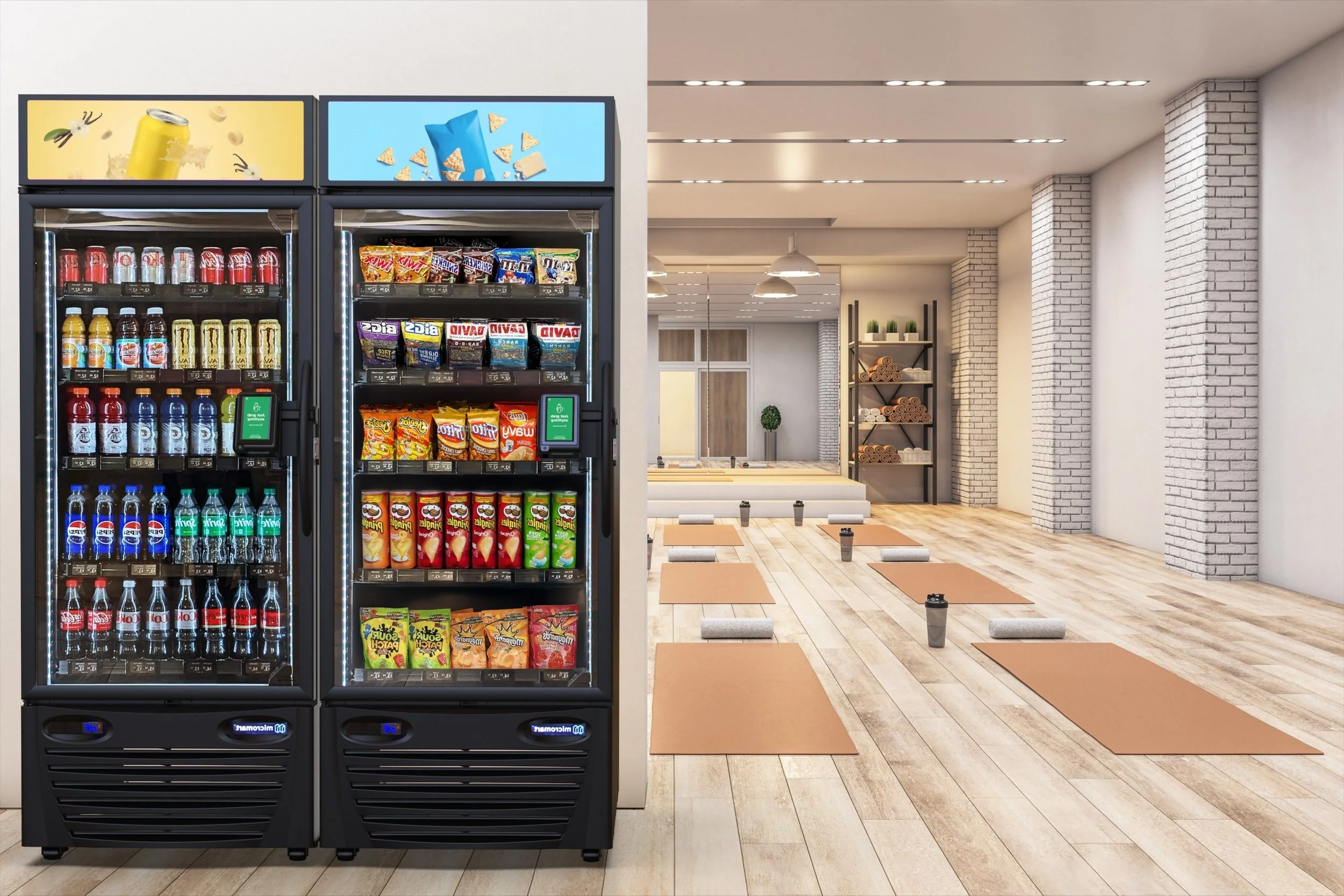Two vending machines with snacks and drinks in a yoga studio with mats and yoga blocks on wooden floor.