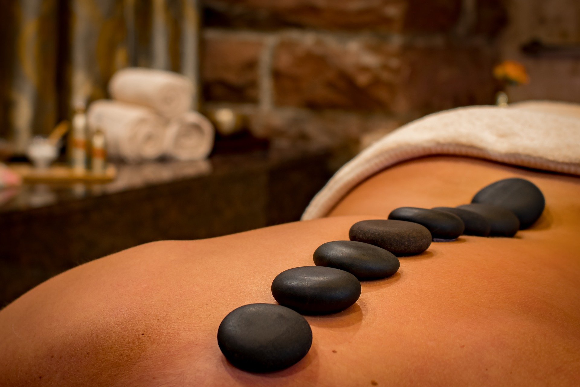 Hot stone massage therapy with black stones arranged along a person's back at a spa.