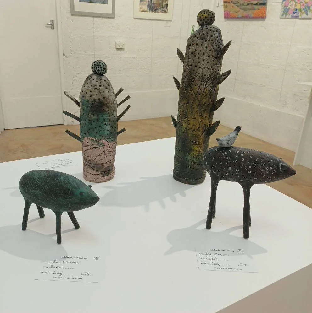 Four abstract ceramic sculptures resembling animals, displayed on a white table in an art gallery. Two sculptures are tall with rounded tops, decorated with dots and protruding shapes, and two smaller sculptures resemble animals with four legs and rounded bodies, decorated with dots.