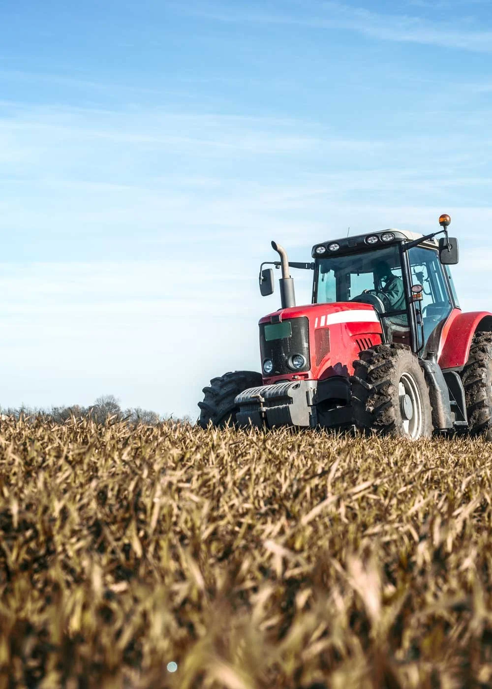 Red tractor on a harvested field with a clear blue sky overhead.