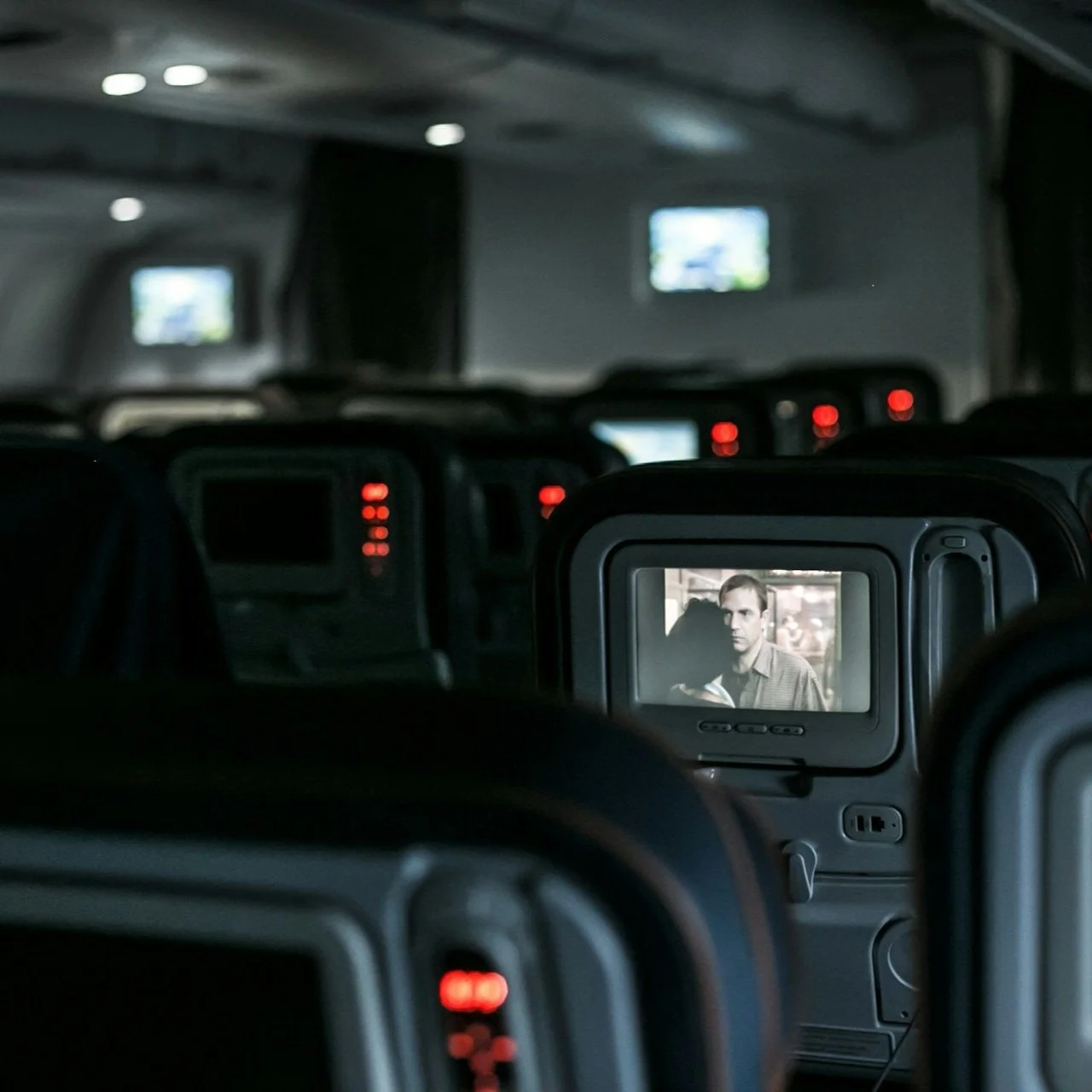 A dark airplane cabin with a movie playing on the seat back entertainment console.