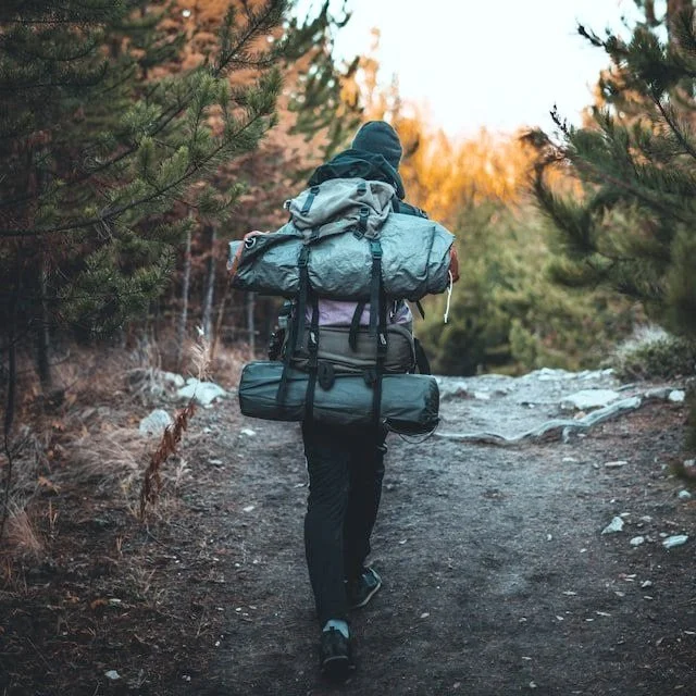 A hiker with a heavy backpack including tents and sleeping bags.
