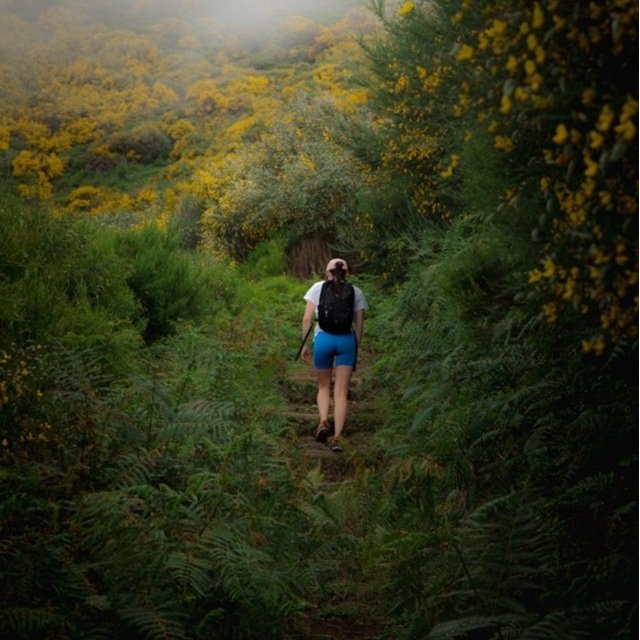 A woman hiking while wearing shorts, a t-shirt, and a sun hat.