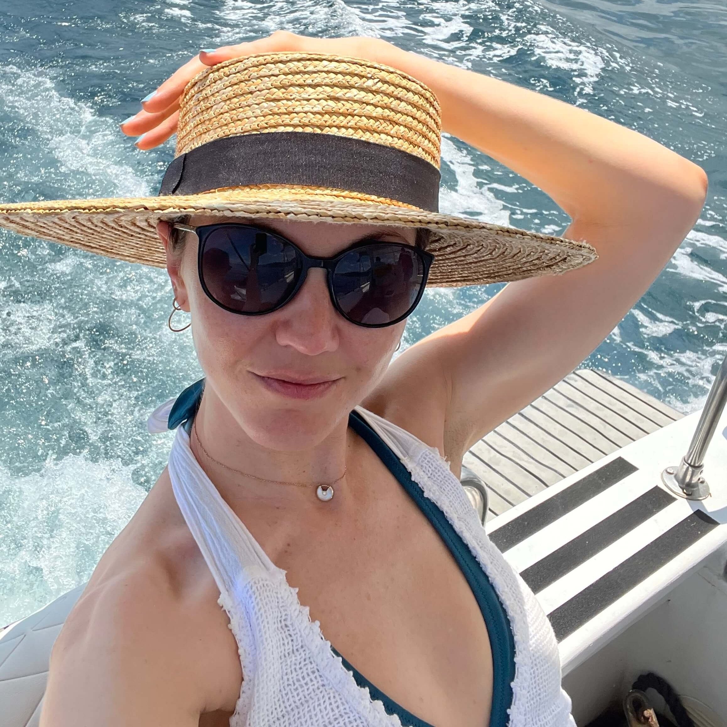 The author on a boat wearing a swimsuit, cover-up, and straw hat.